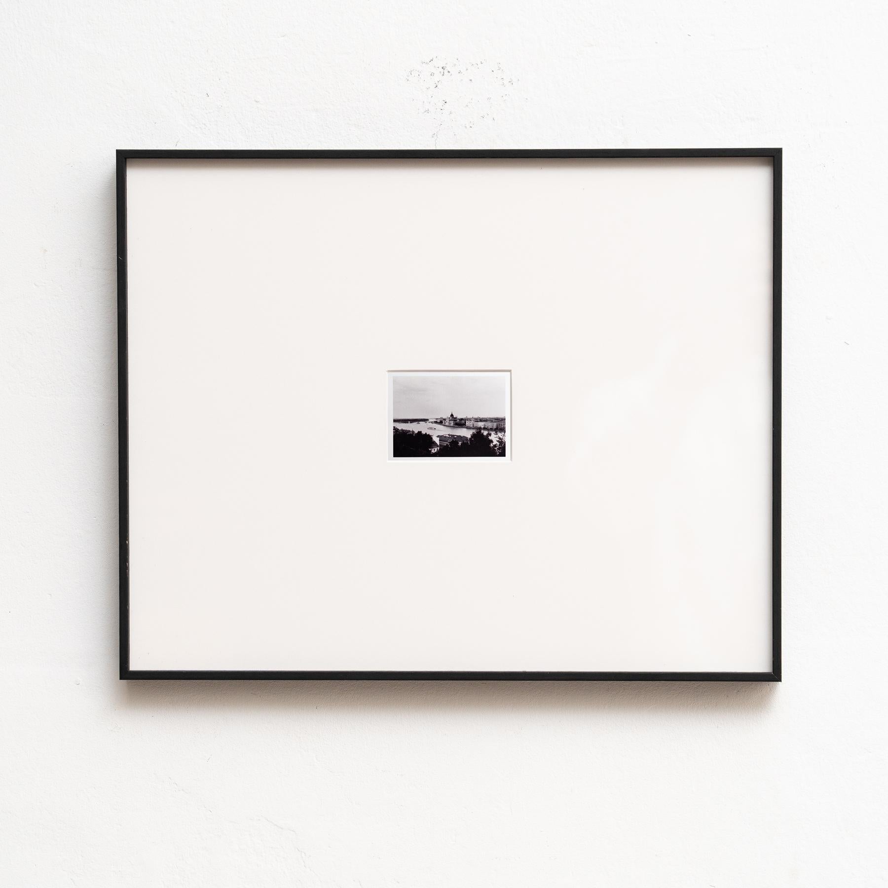 Auf der gerahmten Schwarz-Weiß-Fotografie von Pascal und Vastian entfaltet sich das Stadtbild in einem zeitlosen Panorama mit einem majestätischen Fluss, der sich durch das Herz des städtischen Lebens schlängelt. Der Kontrast zwischen Licht und