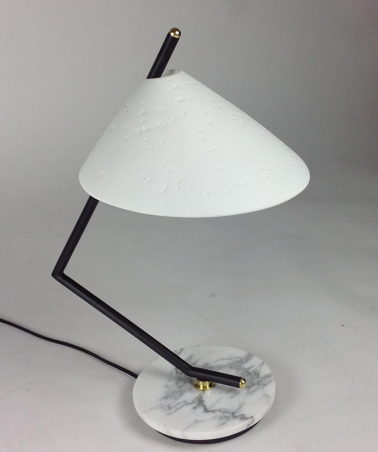 Le mélange de plâtre de Paris, de marbre de Carrera, d'éléments noirs du cadre qui sont accentués par des éléments en laiton, crée une lampe de table saisissante. Avec ses lignes angulaires, le bras de la lampe tient l'abat-jour en plâtre incurvé,