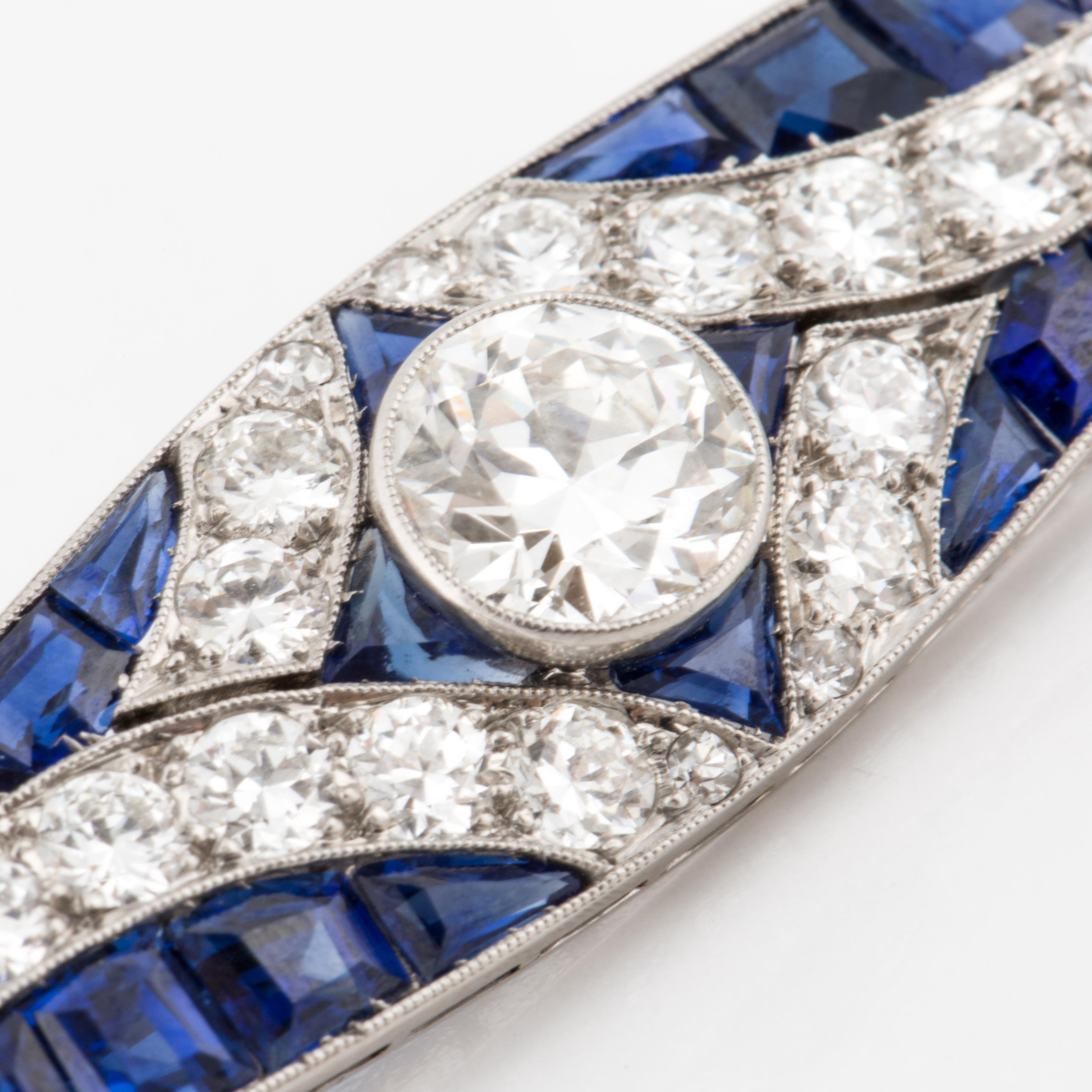 Art Deco bar pin composed of platinum with sapphires and diamonds.  There is one larger Old European-cut diamond in the center of the pin with bead-set diamond accents and calibré-cut sapphires. The center diamond is 1.70 carats, J color, VS1