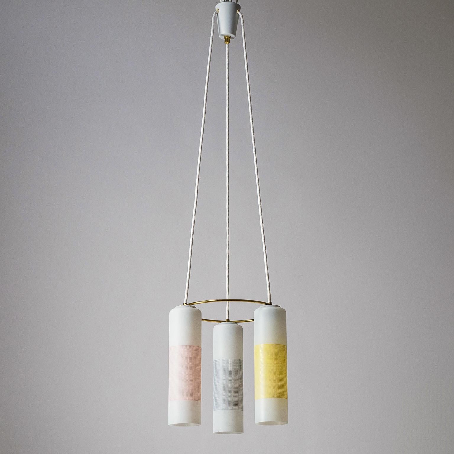 Charming midcentury enameled glass and brass chandelier by Doria Leuchten, Germany, 1960s. Three slender glass tubes enameled in white with geometric decor in pastel yellow, pink and grey. A solid brass ring holds the glasses in position. Fine