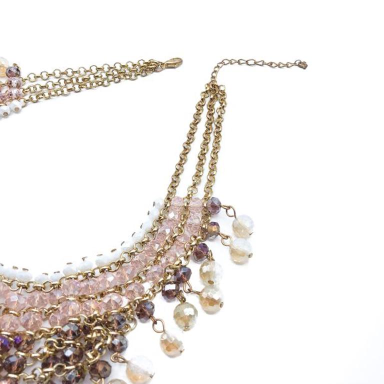 Un collier en verre pastel délicatement coloré. Fabriqué avec des perles de verre de couleur rose pâle, violette et opaline. Métal plaqué or. Il présente un balayage percutant de teintes pastel avec sept rangées de perles reliées par une chaîne en