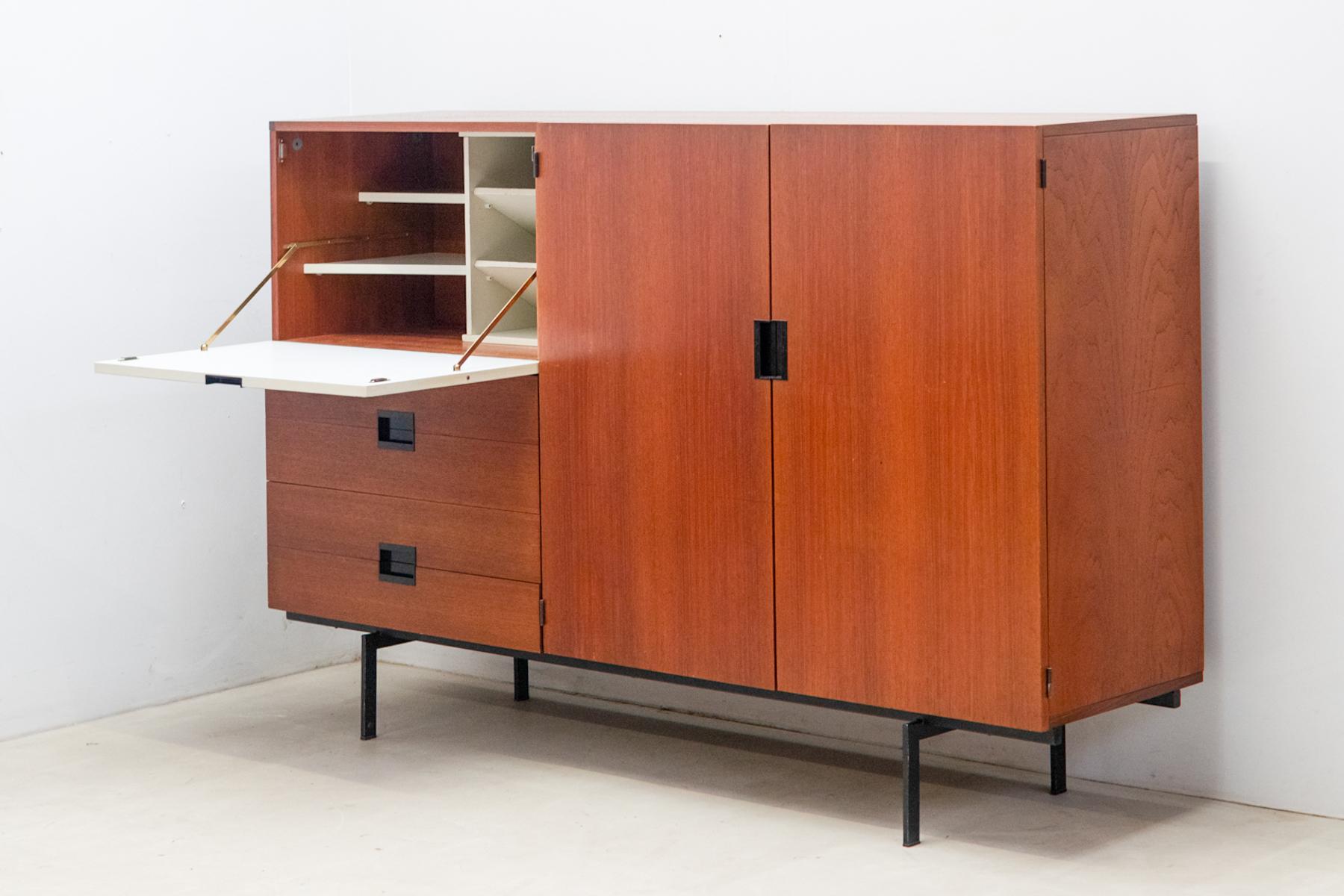 Le meuble haut CU08, conçu par Cees Braakman pour Pastoe en 1958, est fabriqué en bois de teck et doté d'une porte pliante laquée blanche. 
Il comprend également quatre tiroirs en dessous et deux portes à droite. 
Faisant partie de la série