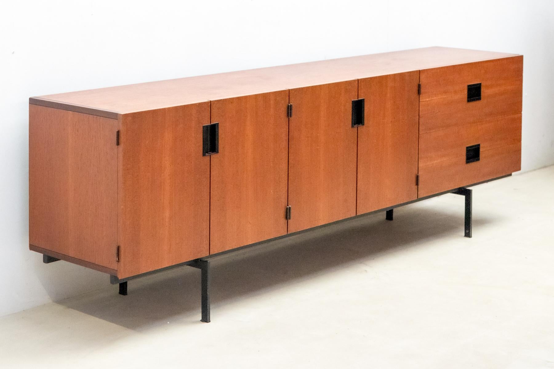 The minimalist sideboard DU03, designed by Cees Braakman for Pastoe in 1958, is a Dutch design classic.
 Crafted from teak wood, it features a sleek black lacquered metal frame. 
The cabinet is adorned with black plastic Japanese-style grips, a