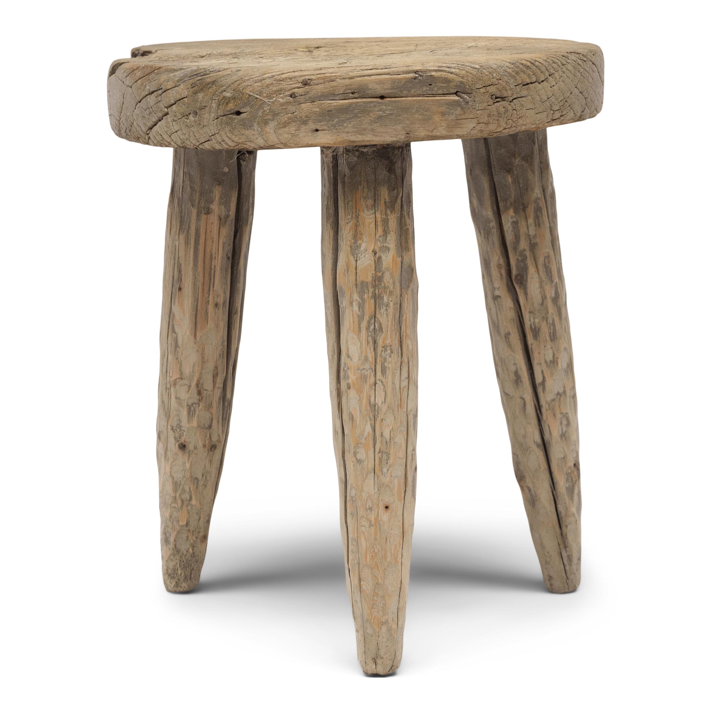 The round top of this rustic, tri-leg side table is an antique wooden cart wheel, repurposed from an early 20th century ox-drawn wagon or farm cart. Rich with character, the wheel is textured by deep grooves that follow the swirling grain and marked