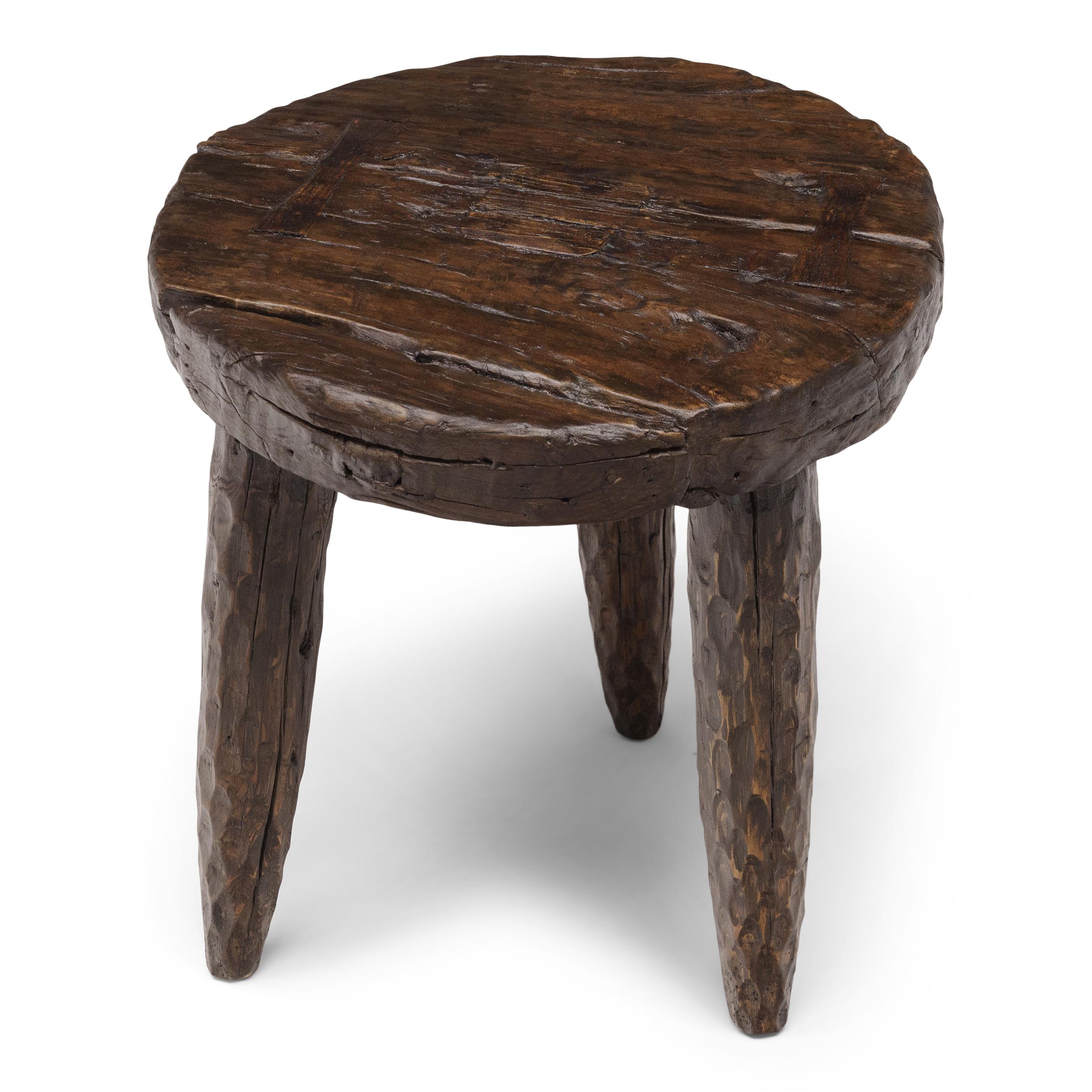 The round top of this rustic, tri-leg side table is an antique wooden cart wheel, repurposed from an early 20th century ox-drawn wagon or farm cart. Rich with character, the wheel is textured by deep grooves that follow the grain pattern and marked