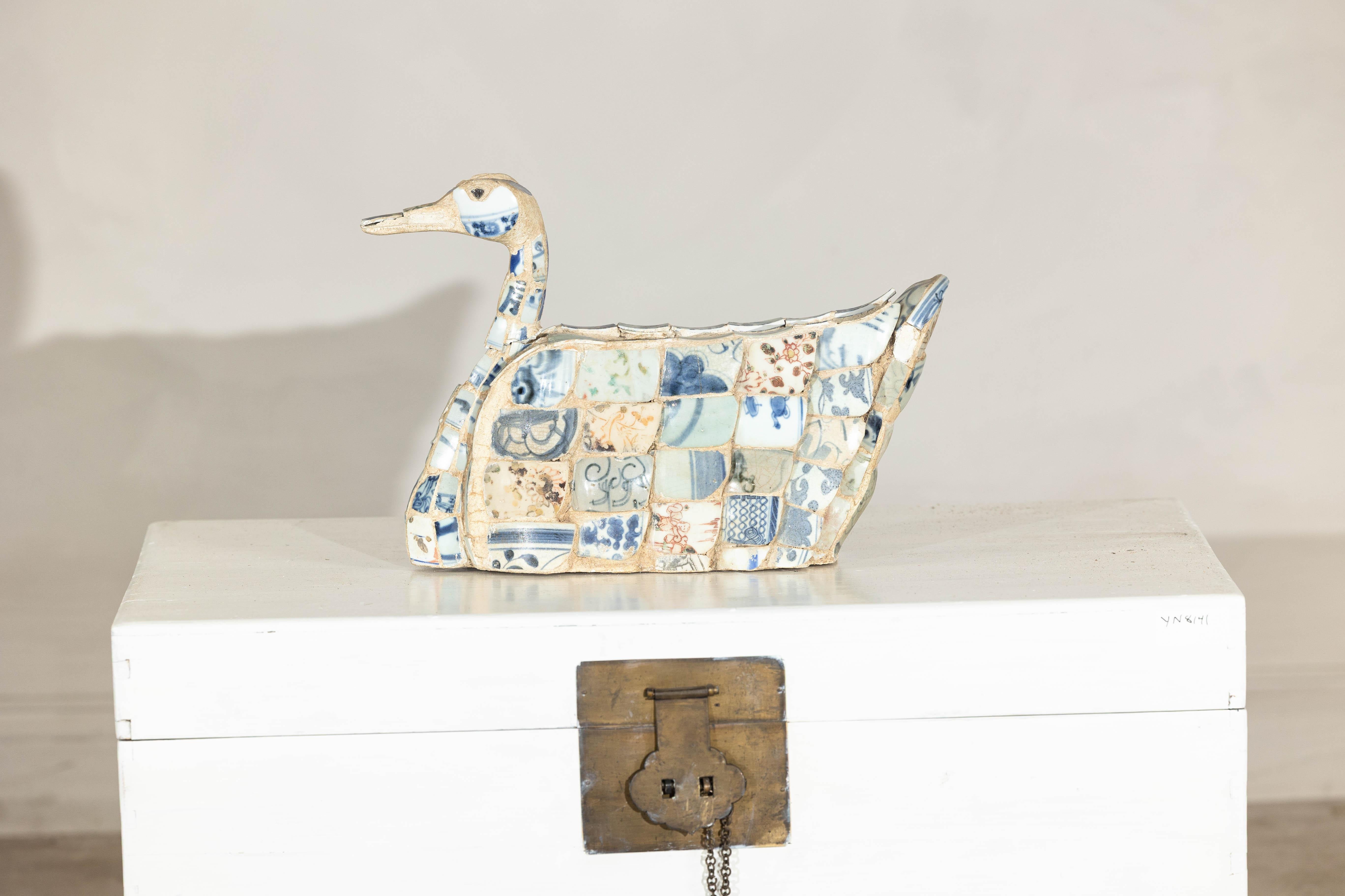 This unusual sculptural duck is crafted from a mosaic of antique Chinese porcelain fragments, likely salvaged from Qing dynasty export wares. The assembled shards are predominantly blue and white, featuring underglaze decoration with scrolling