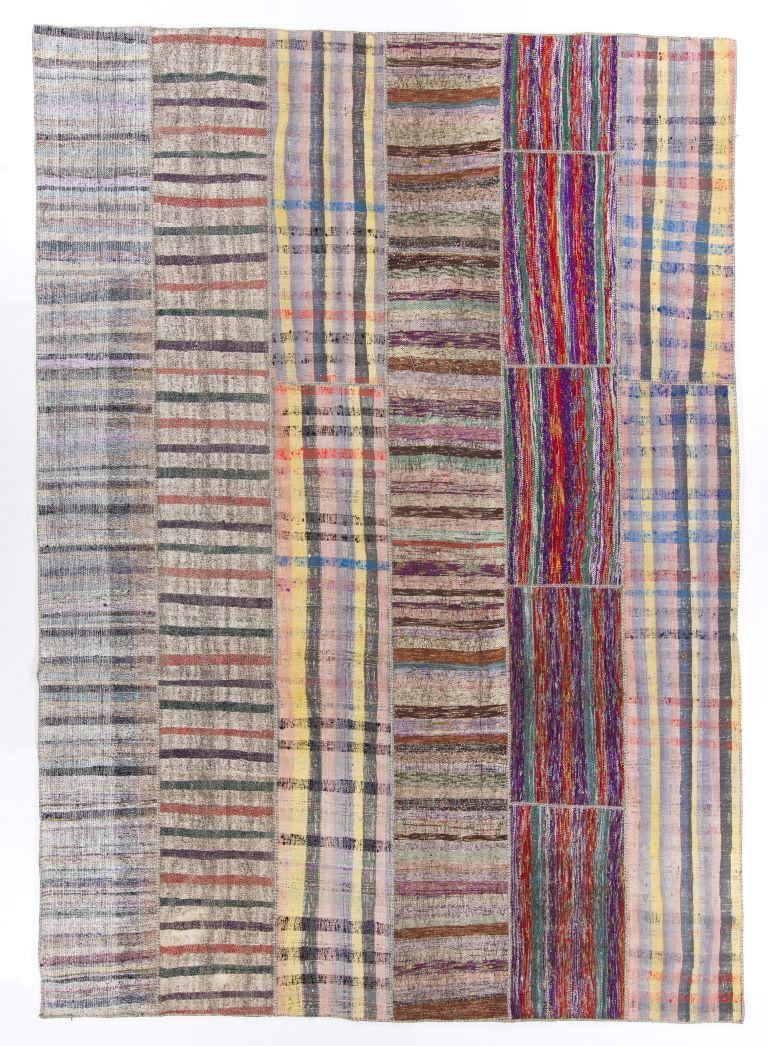 A large decorative Turkish flat-weave/kilim patchwork rug with a minimalist aesthetic made up of hand-woven and hand-stitched vintage kilim pieces that feature various striped designs in a color palette of vivid, pastel and earthy colors. It is made
