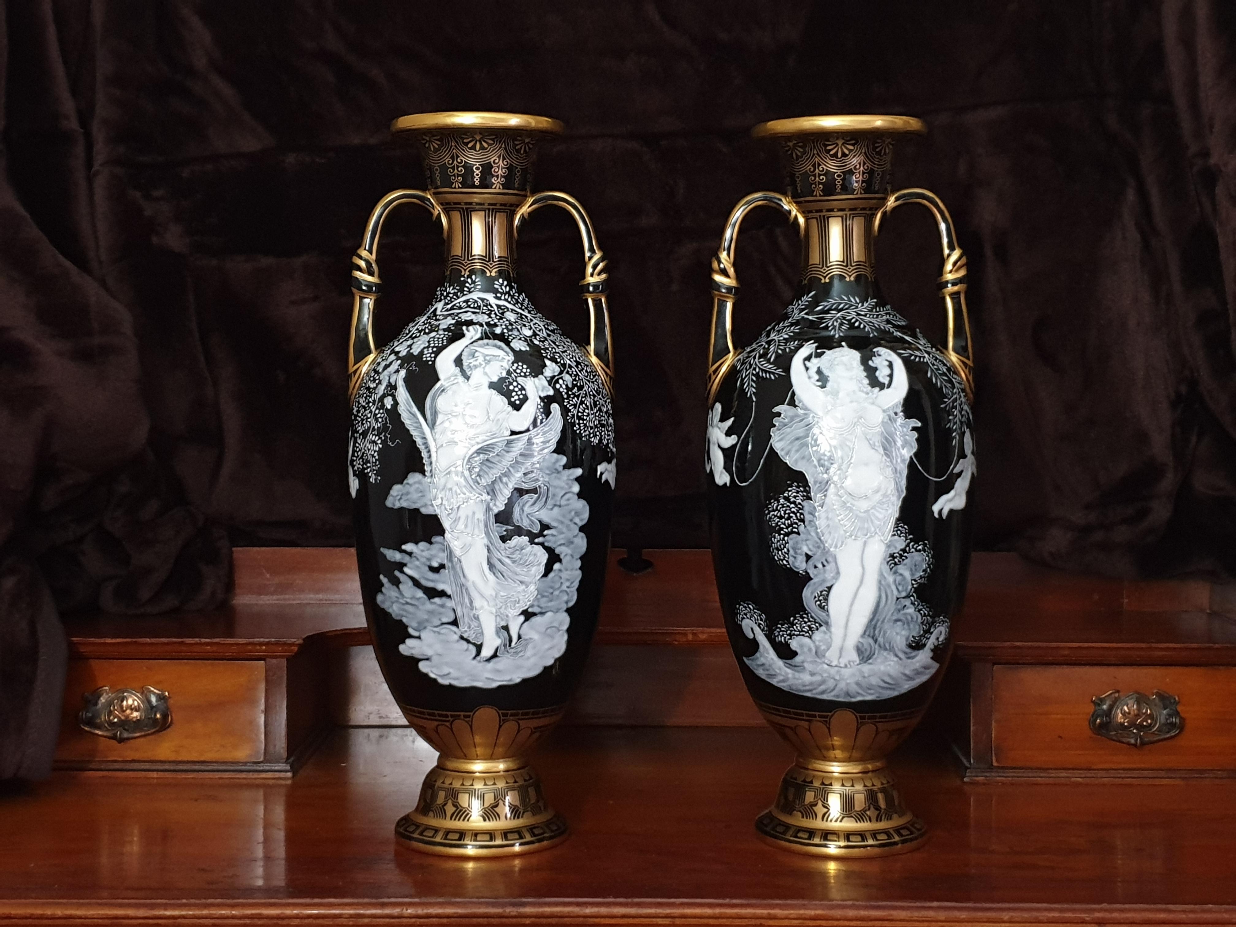 A magnificent pair of 'pate-sur-pate' twin handled vases, circa 1880. The loutrophoros shaped vases each worked with scantily clad maidens interspersed with winged putti amongst foliate sprays, the neck handles and foot feature geometric gilt
