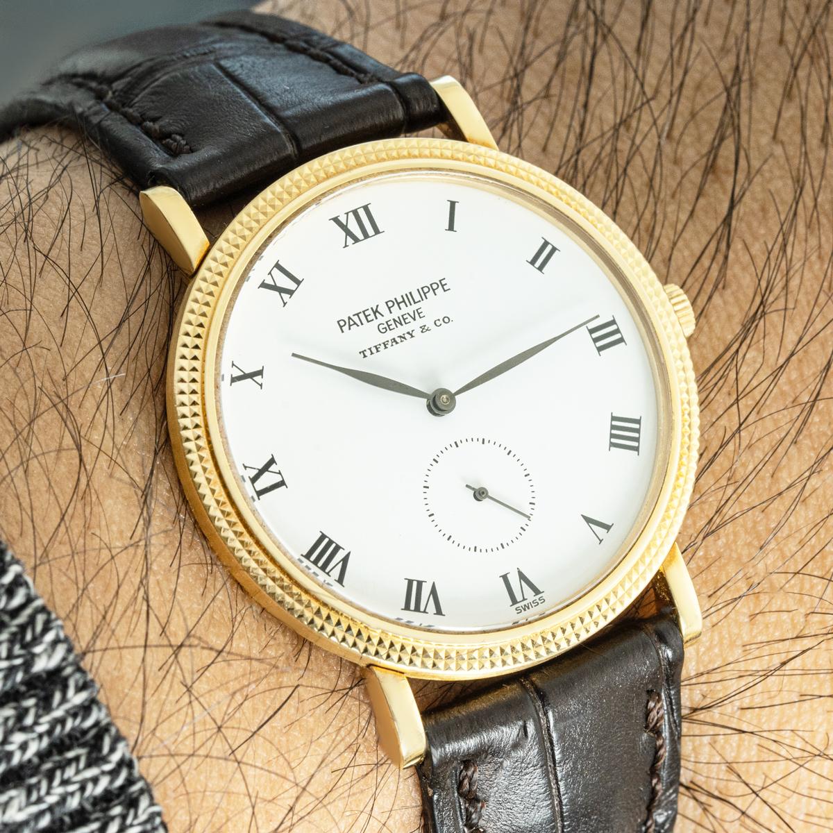 A gentlemen’s Patek Philippe Calatrava wristwatch crafted in 18k yellow gold, featuring a white porcelain dial signed by both Patek Philippe and Tiffany &Co. The dial showcases elegant black Roman numerals, traditional leaf-shaped hands, and a small