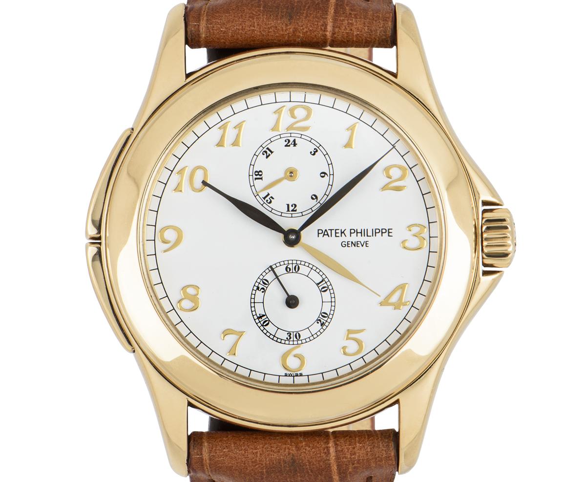 A 37 mm Calatrava Travel Time with complications in yellow gold by Patek Philippe. Features a white Arabic dial with a second time zone hand, a 24 hour display and a small seconds display. The brown leather strap is generic, equipped with a yellow