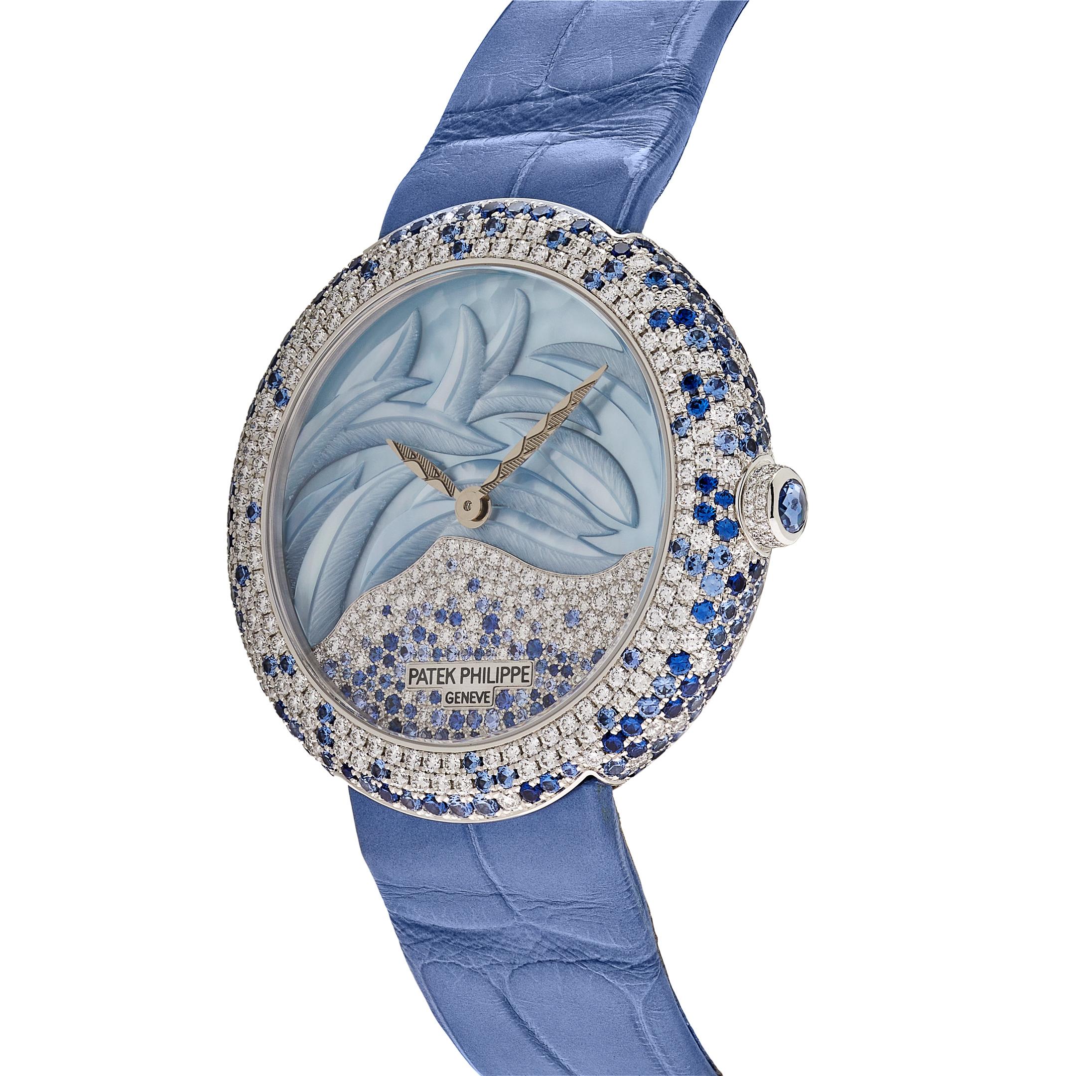 The Patek Philippe Calatrava watch features a 38.5mm white gold case on a blue alligator leather bracelet with a gem-set prong buckle. On the lower part of the dial, diamonds mingle with blue sapphires in a “random” or “snow” setting, while the