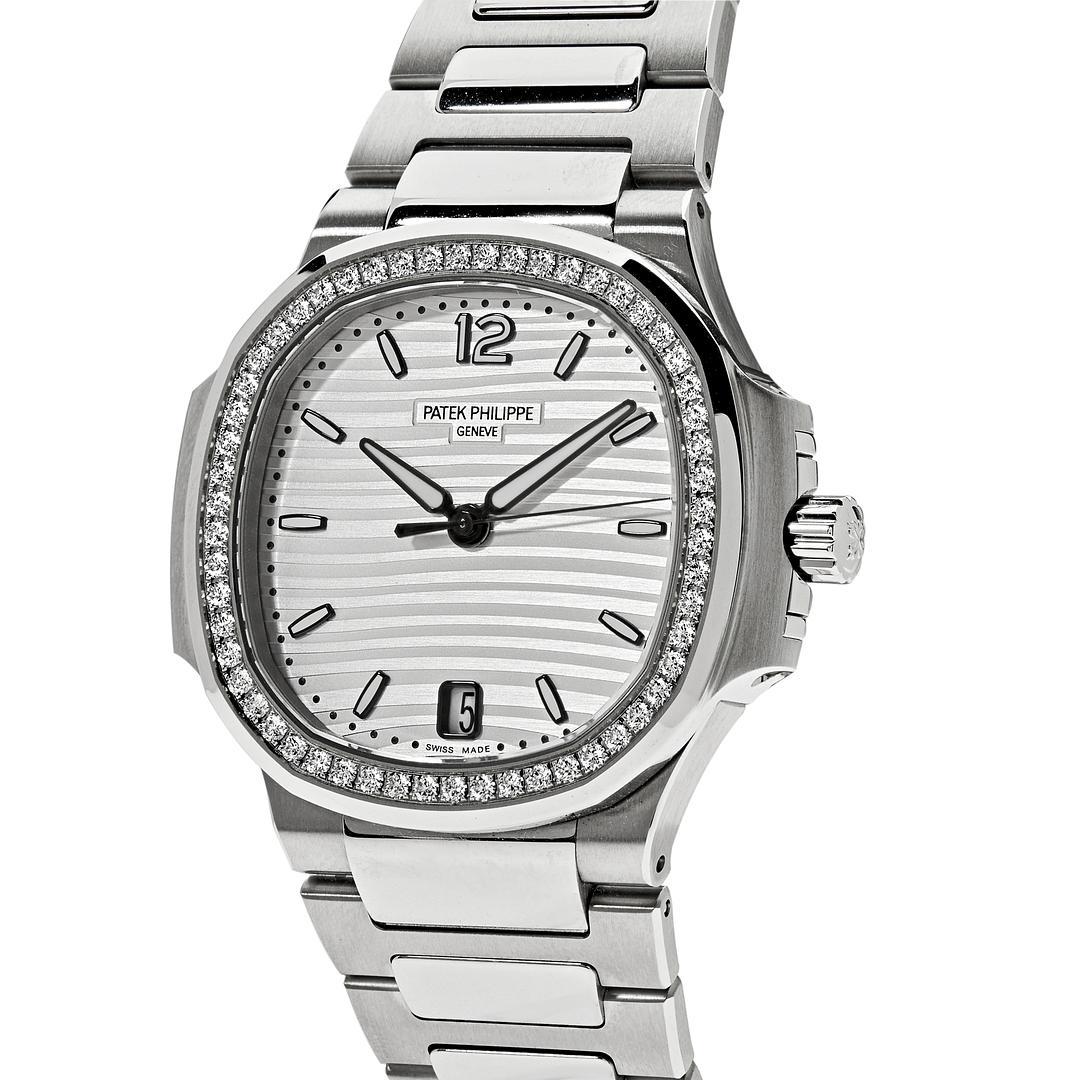 The Patek Philippe Ladies Nautilus wristwatch features a round octagonal shape diamond-set bezel and 35mm stainless steel construction. In the center, lays a white embossed dial with gold applied numerals and hour markers. It is finished with a