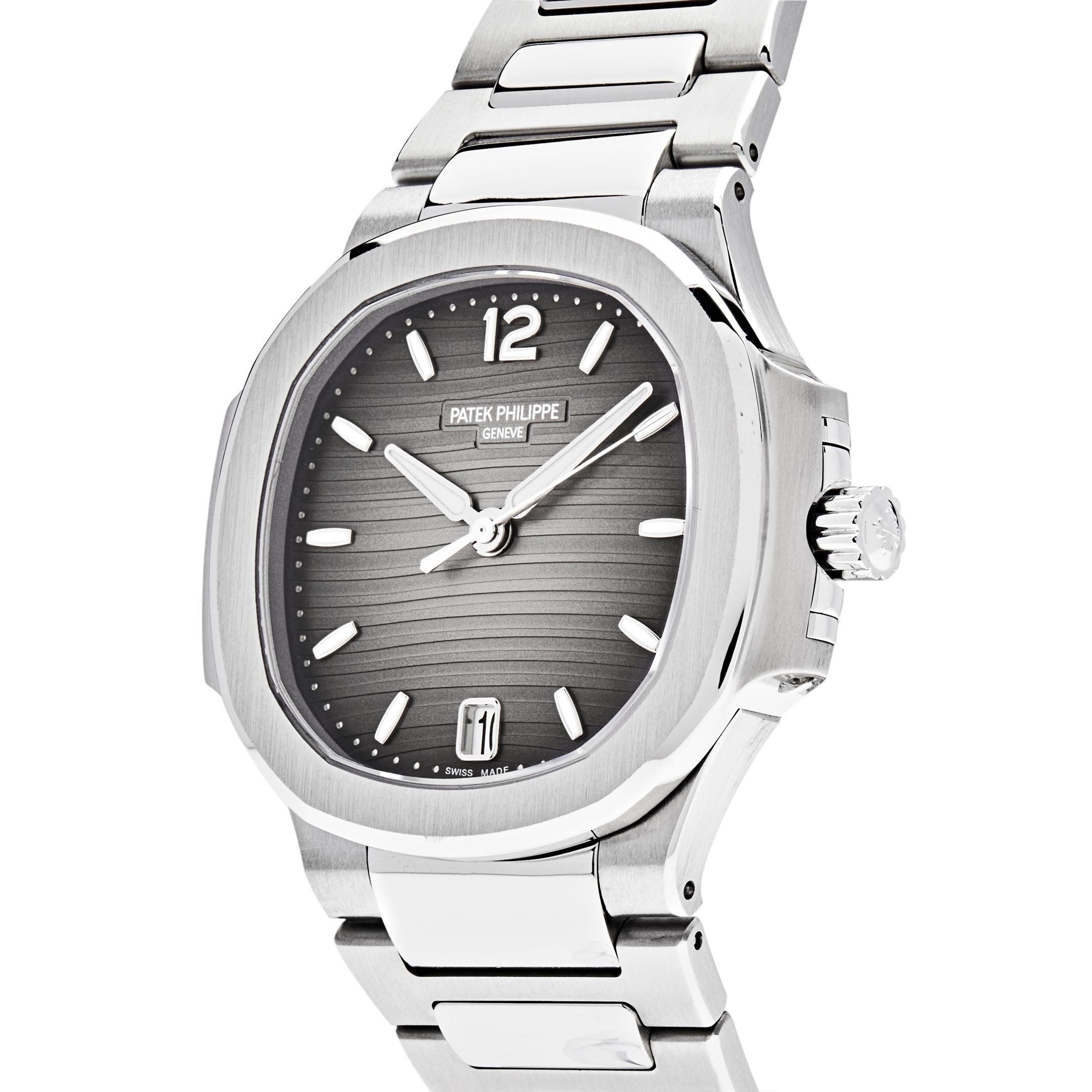 This Patek Philippe Ladies Nautilus wristwatch features a 35mm stainless steel case and bezel. In the center, lays a smoke grey dial with gold applied numerals and hour markers. It is finished with a stainless steel bracelet and fold-over clasp