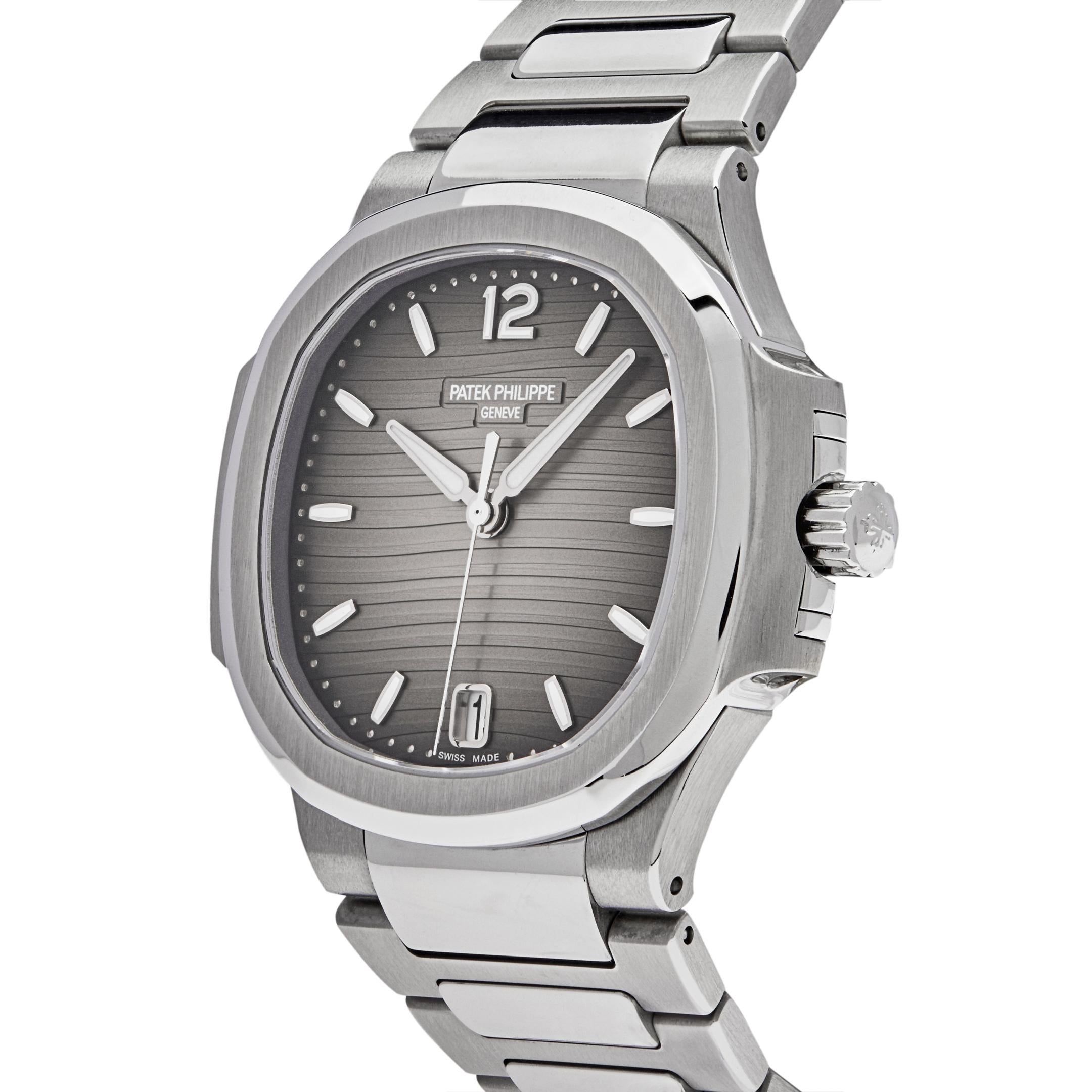 The Patek Philippe Ladies Nautilus features a round stainless steel bezel and 35mm stainless steel case. In the center, lays a smoke grey dial with gold applied numerals and hour markers. It comes on a stainless steel bracelet with a fold-over clasp