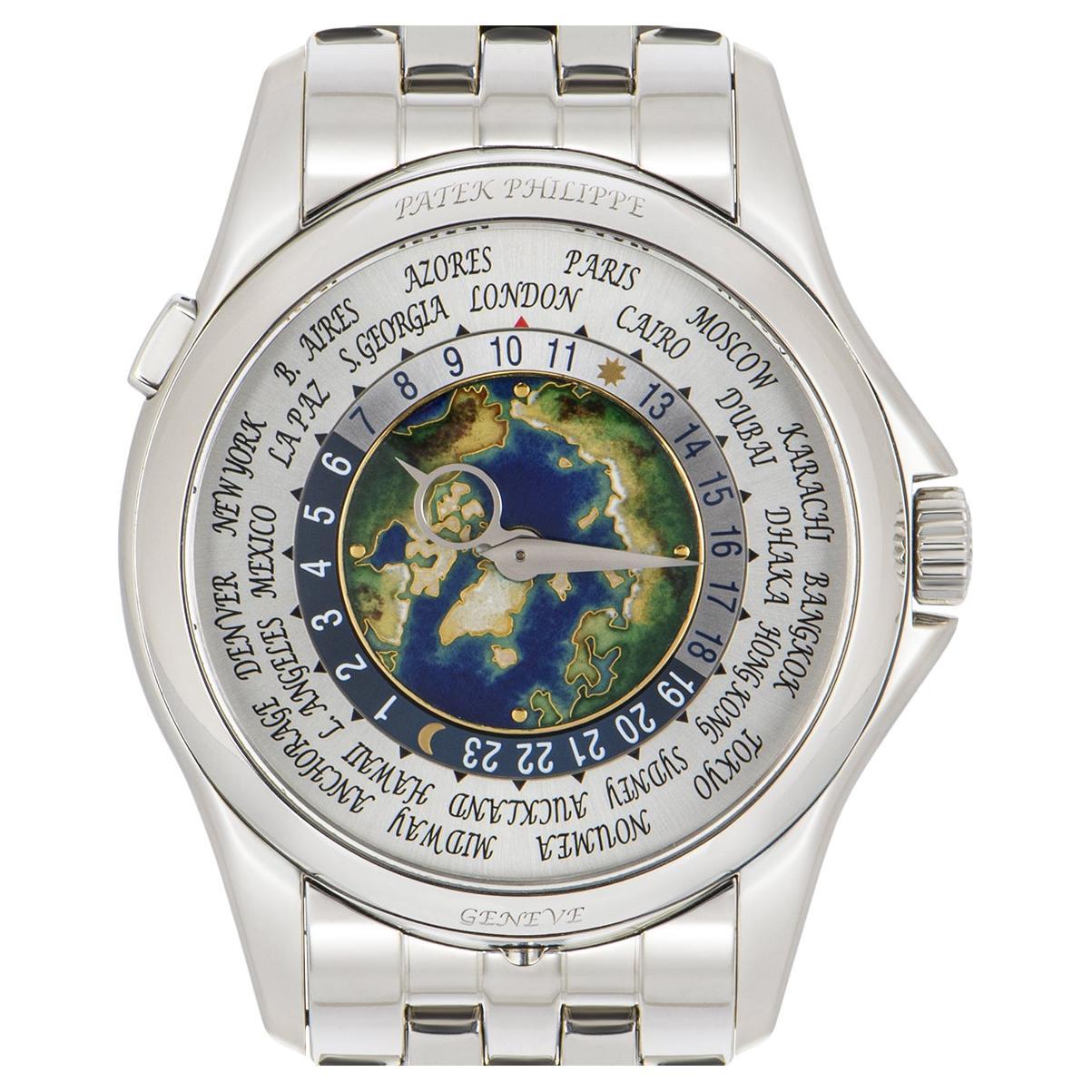 A platinum World Time with complications by Patek Philippe. Featuring a silver dial with a cloisonne enamel centre. The dial itself features a 24-hour display and the time of 24 worldwide locations. Set just beneath the case at 6 o'clock is a single