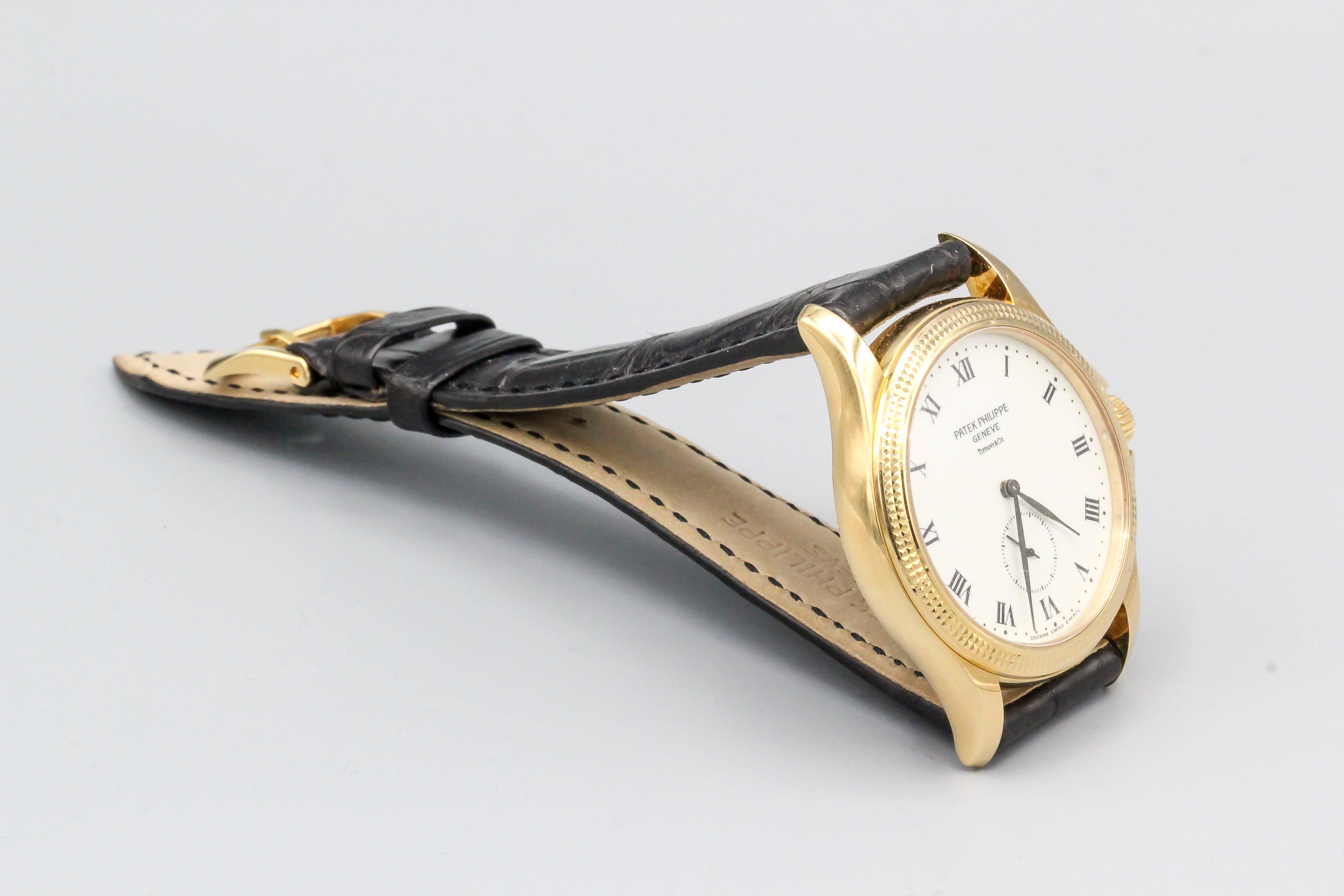 Fine 18K yellow gold wrist watch by Patek Philippe & Co. for Tiffany & Co., reference # 5115. It features a double-signed enamel dial, 18k gold case with hobnail bezel, 18k gold tang buckle, genuine new Patek Philippe coffee brown strapstrap, and a