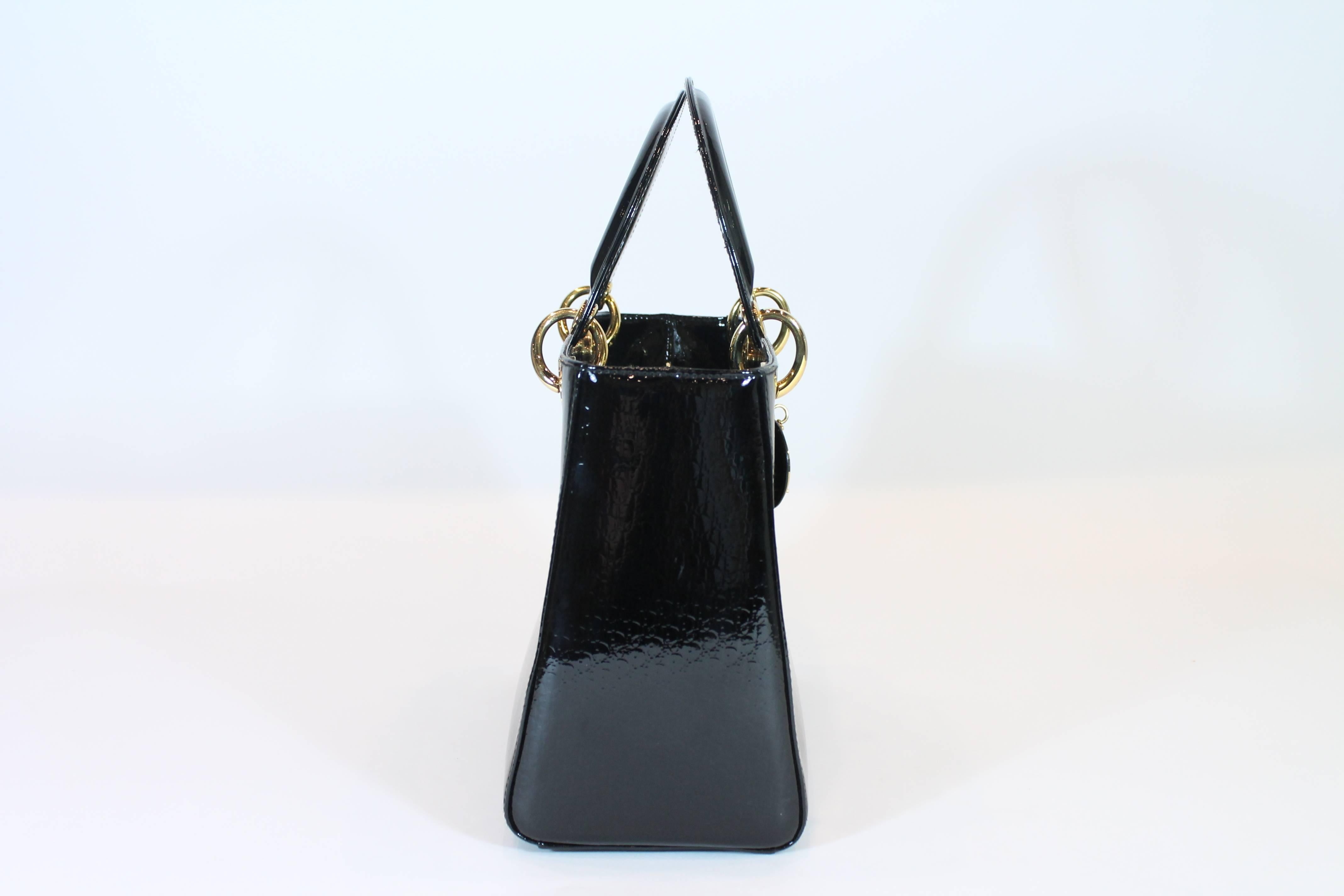 Black patent leather. Gold-tone hardware. Dual top handles. Zippered closure at top. One interior zippered pocket.