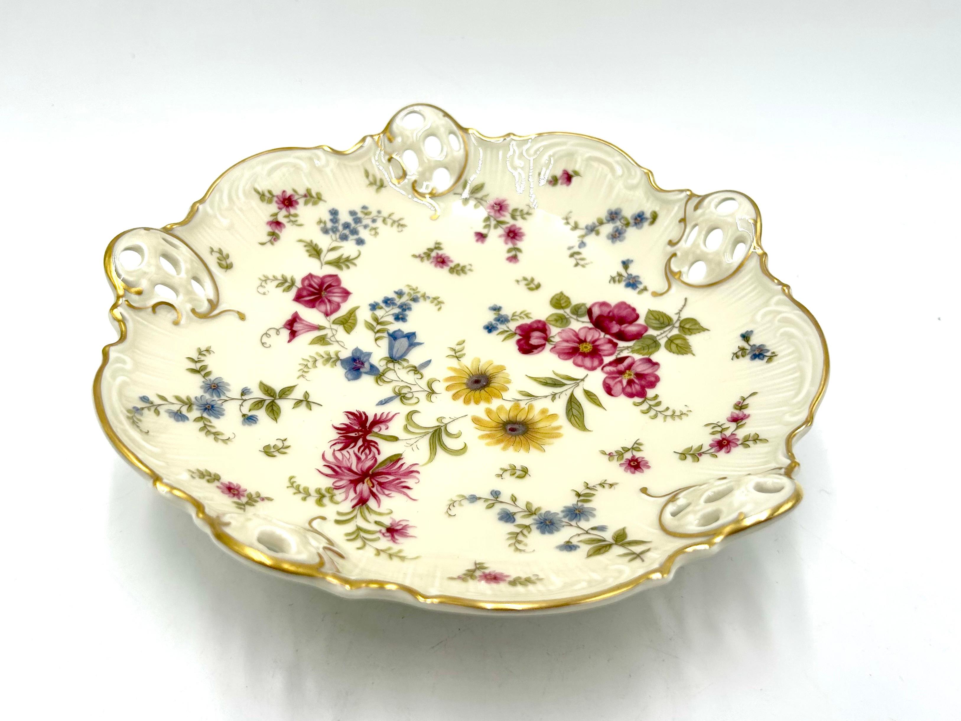 Openwork plate supported on three filigree legs from the Moliere collection, the renowned German Rosenthal label. The product is marked with the mark used in the years 1938-1952. Ecru porcelain decorated with openwork sides, floral meadow motif and