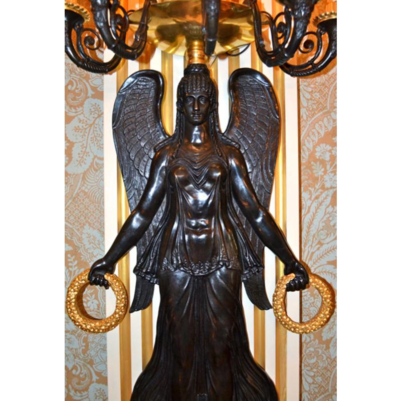A pair of monumental French Empire style wall sconces in finely chased, patinated and gilded bronze. The large winged Victory stands on a gilded globe, studded with stars, holding a gilded wreath in each outstretched hand. Atop her head sits a