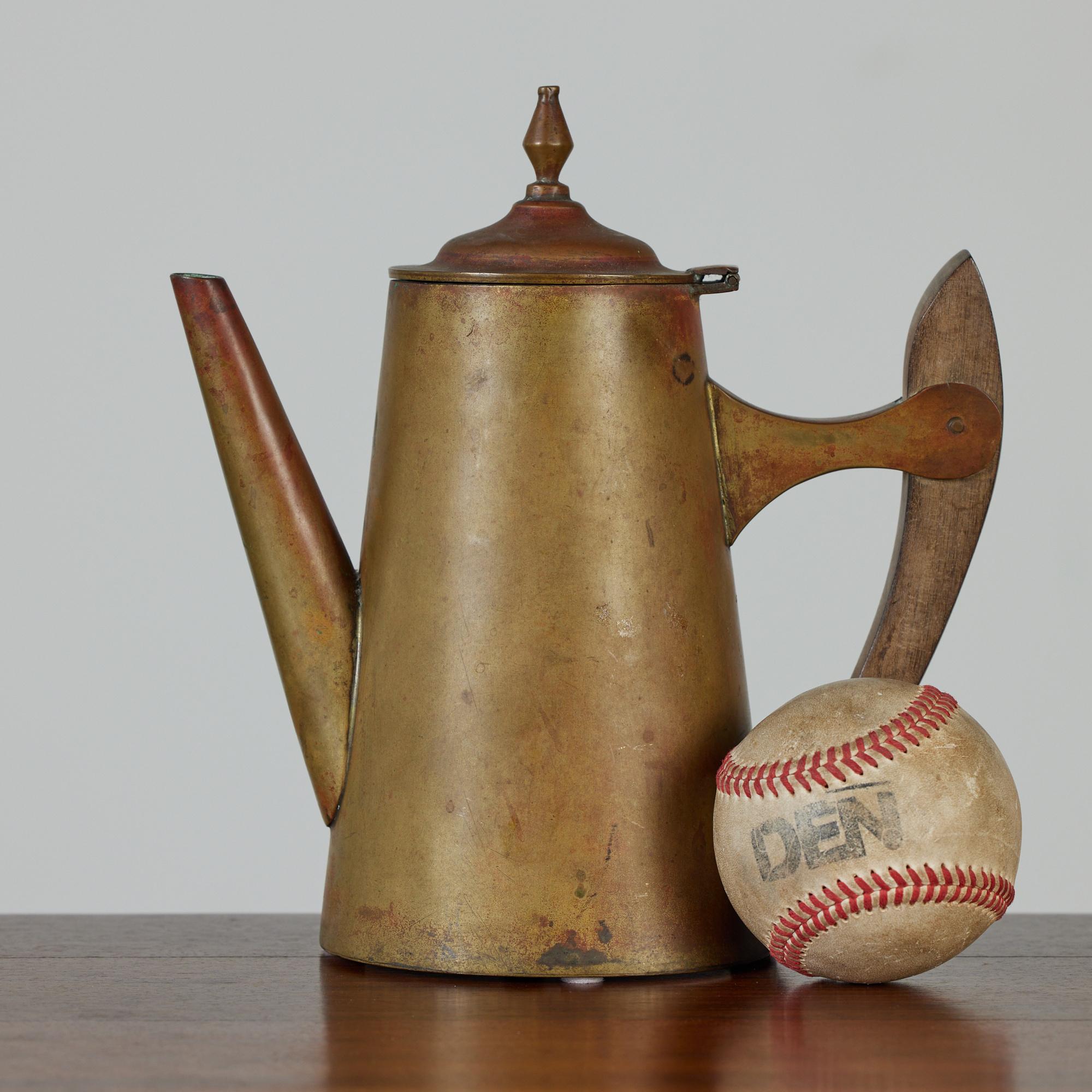 This tall teapot features a gorgeous patinated brass and a sculptural weathered wood handle. The hinged lid has a diamond shaped spindle on its top. The pot would be a lovely collectible to add to your kitchen décor or any shelf needing a little