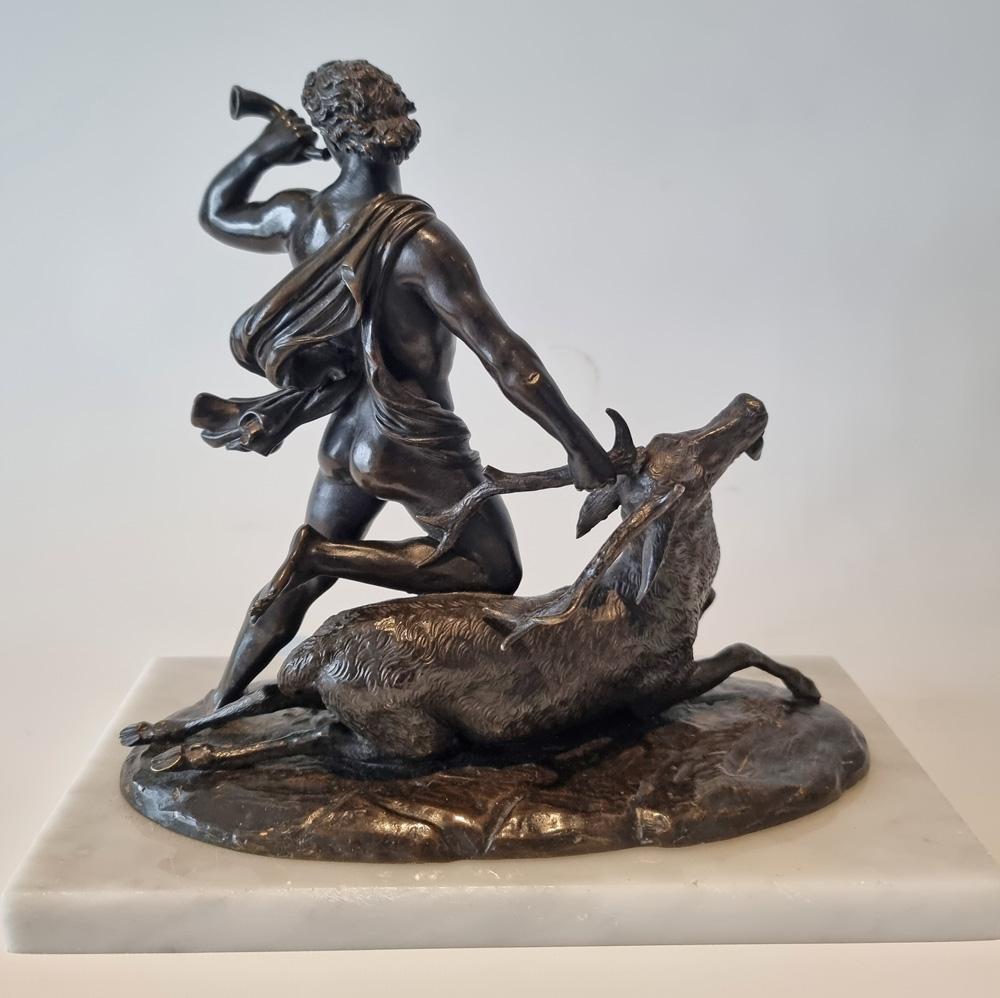 Patinated Bronze model of a huntsman and a stag, possibly Hercules and the Ceryneian stag by Holme Cardwell. Depicting a Classical figure wearing a flowing cloak and holding a stag by the antler with his right hand while blowing a trumpet with his