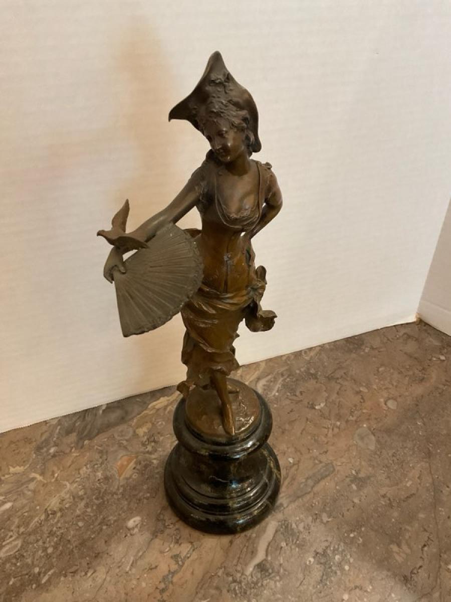 This listing features a bronze patinated cast sculpture of a female figure dressed in Rococo-style attire with a traditional folding fan and a small bird. This sculpture's origins are unknown, but based on the style of dress it likely was sculpted