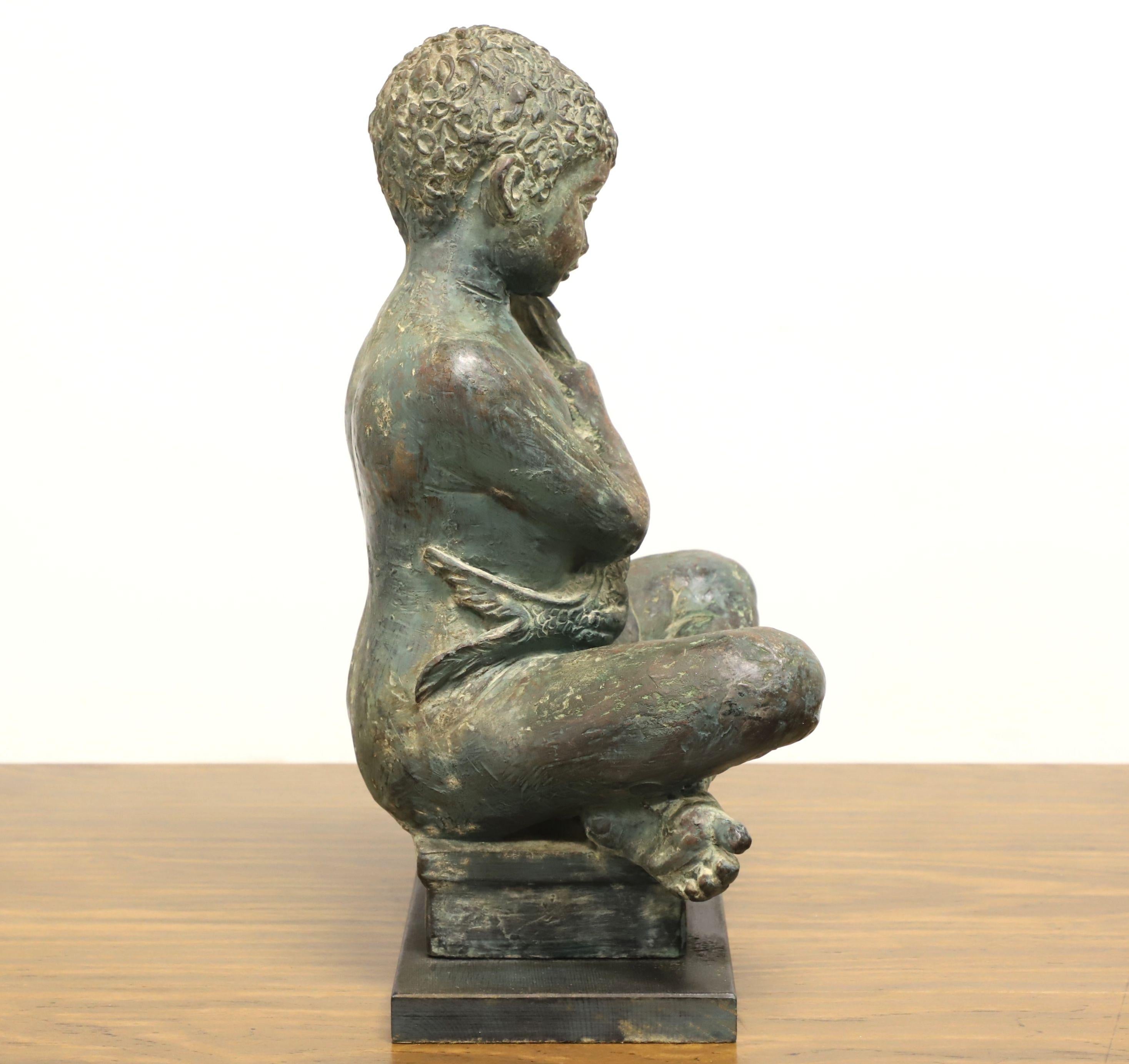 A patinated bronze sculpture depicting a boy seated cross legged on a cushion holding a fish. Unsigned, artist unknown. Solid bronze with patinated green tone and on bronze base. Origin unknown, likely Mediterranean region, and produced in the mid