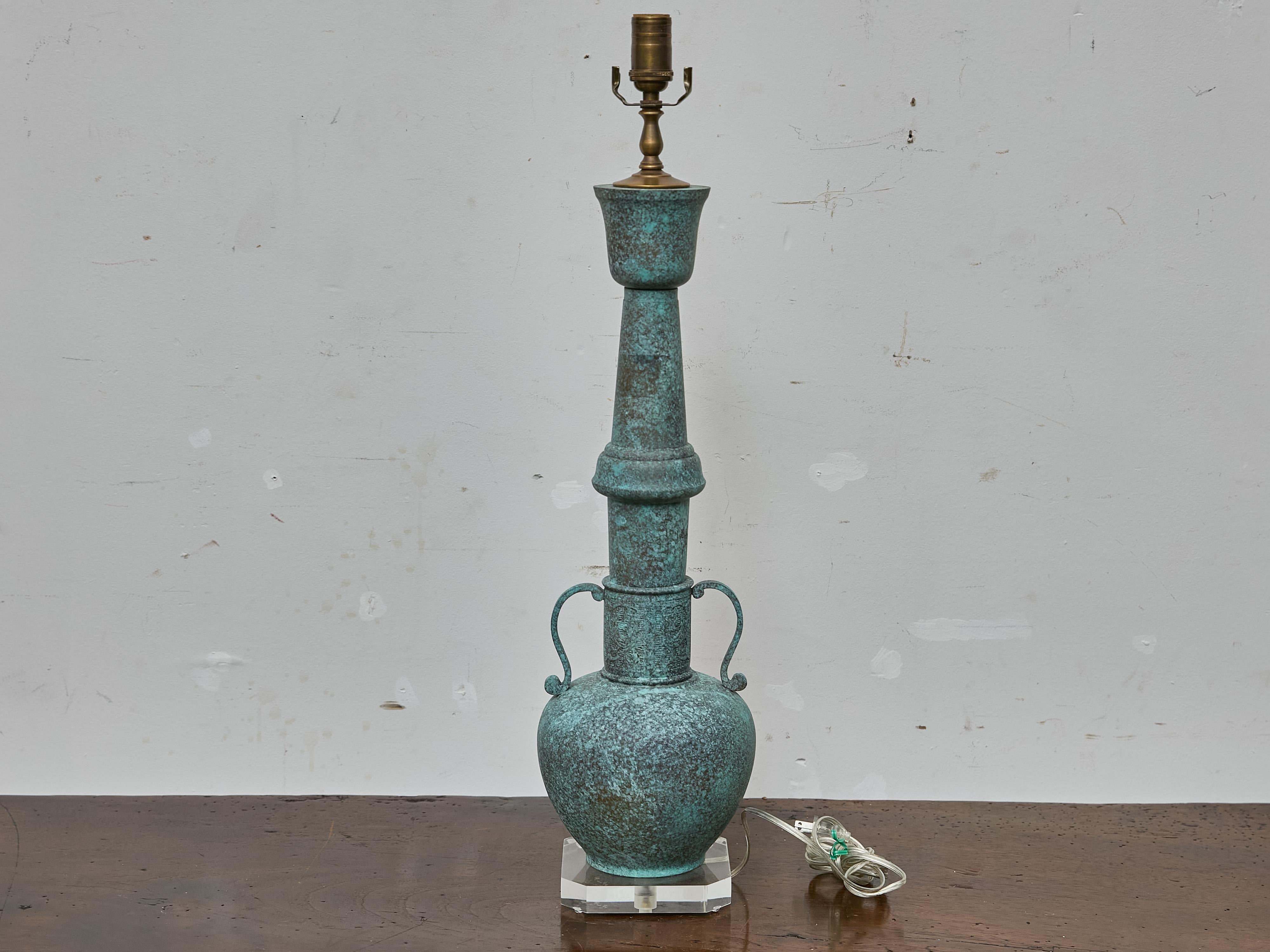 This tall bronze table lamp is crafted in the bold, sculptural style associated with James Mont, a designer known for blending Eastern and Western influences into dramatic, decorative forms. The lamp features a distinctive elongated silhouette with