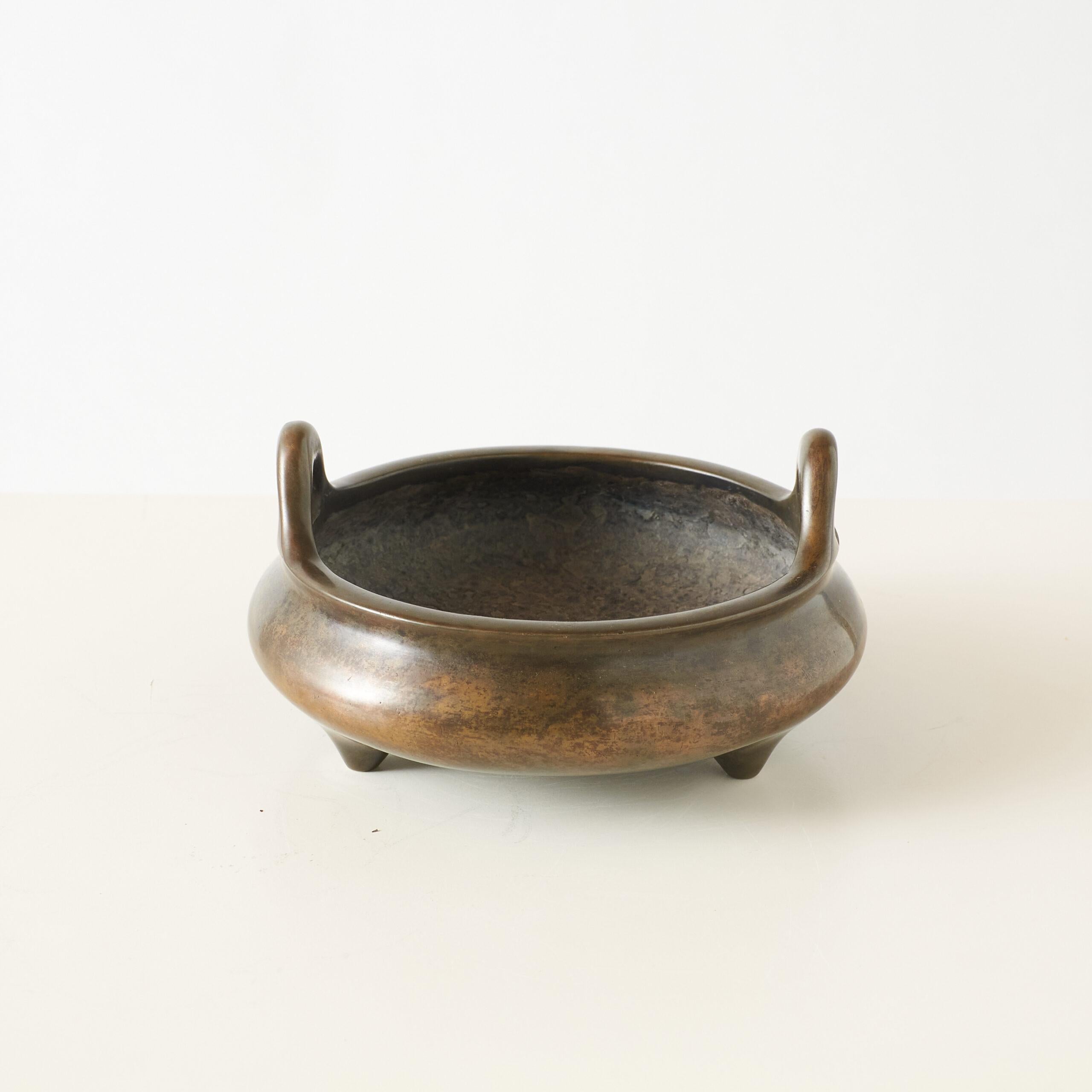 Patinated Bronze Tripod Censer with Double Handles

Round bronze censer with three legs and upright double handles at the rim. The surface shows a smooth, aged patina. Marked on the base with Da Ming Xuande Nian Zhi (大明宣德年製) in seal script,