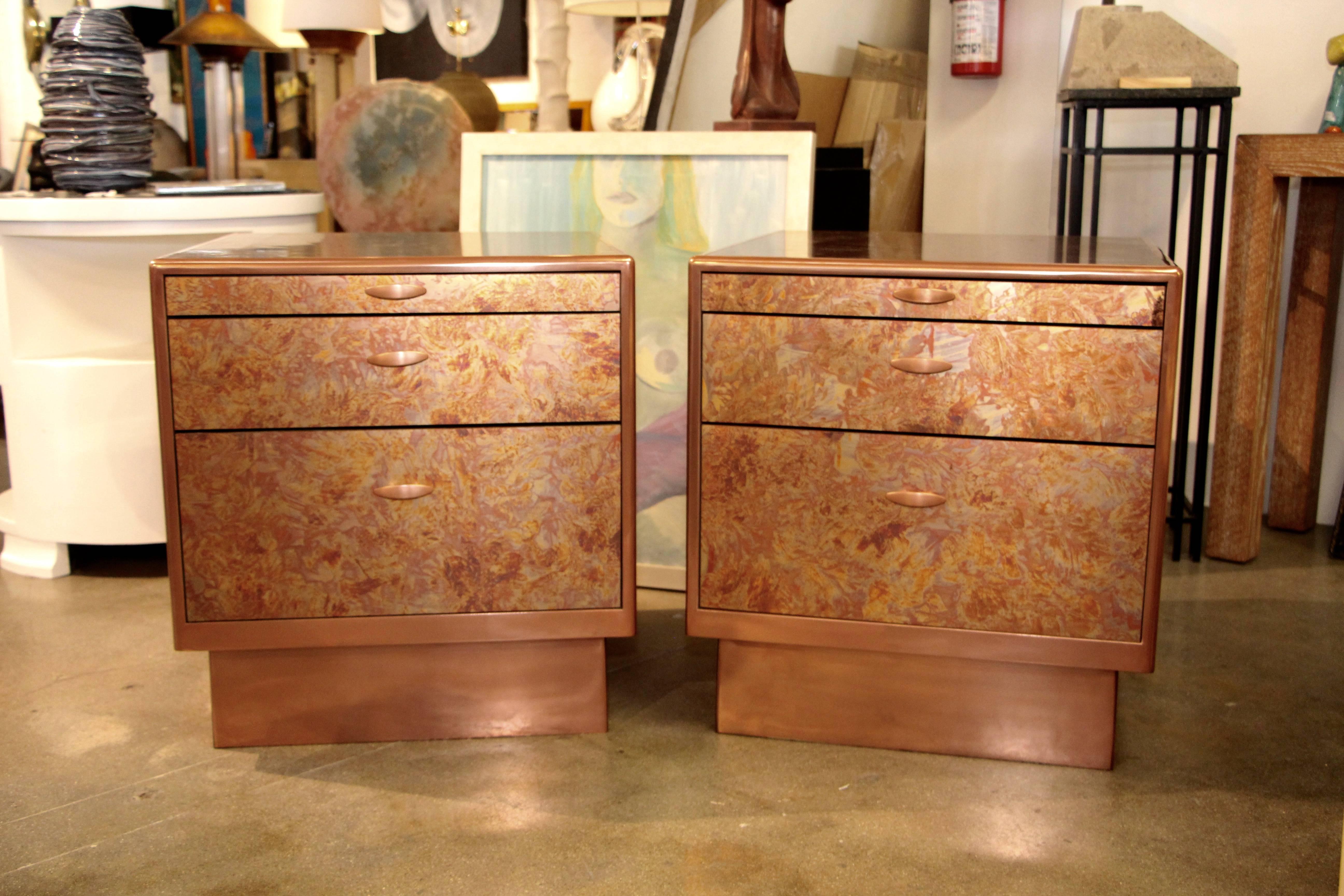 A beautiful pair of nightstands or end tables with patinated copper sheets on top front and side. The bases have been coated in copper metal as has the trim and handles. The top drawer is actually a pull out tray. The other two drawers are actually