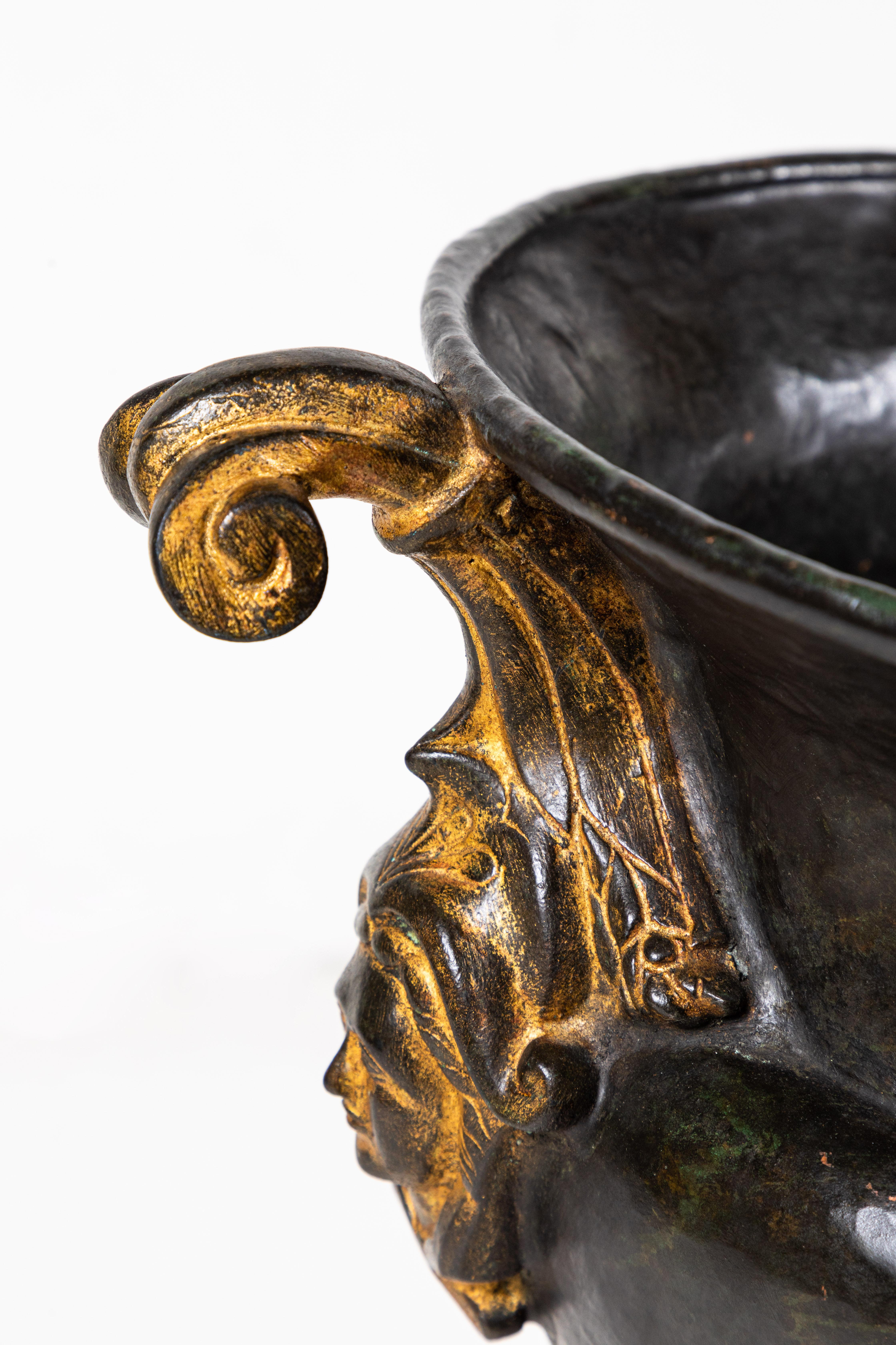 Chic, large, hand-cast, circa 1950, patinated, Italian, bronze urn atop a stepped foot. The body embellished with scrolling armatures featuring relief portraits.