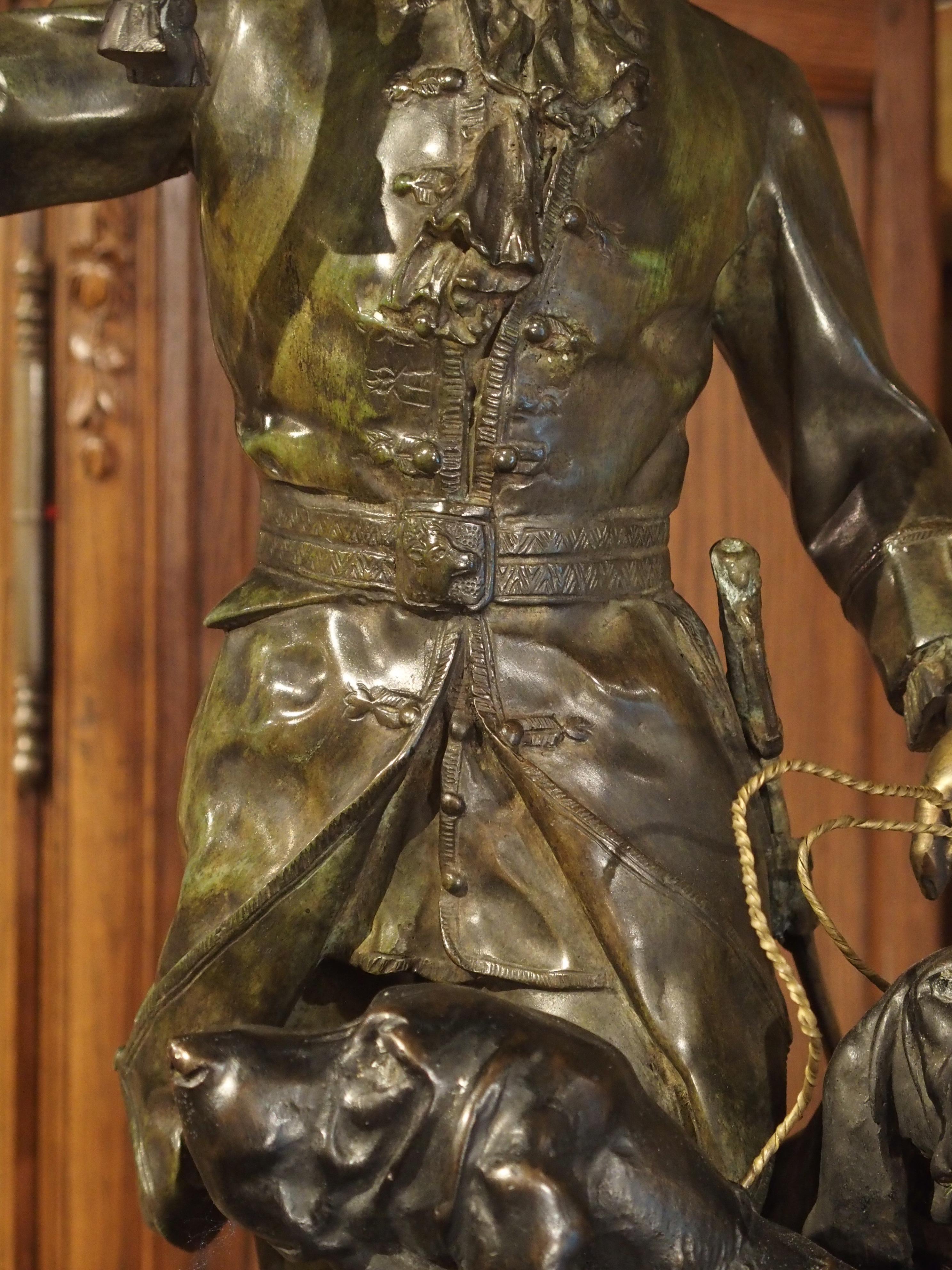 20ième siècle Statue française en bronze patiné représentant un chasseur et des chiens de chasse sur un piédestal en marbre