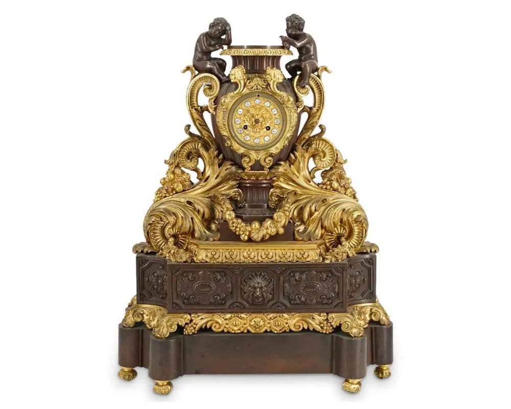 An antique patinated and gilt bronze mantel clock with Christofle movement. Case features an urn form with double figural cherub mounted acanthus leaves, further decorated with hanging fruit adorned weathers, and ornate ornamental reliefs along