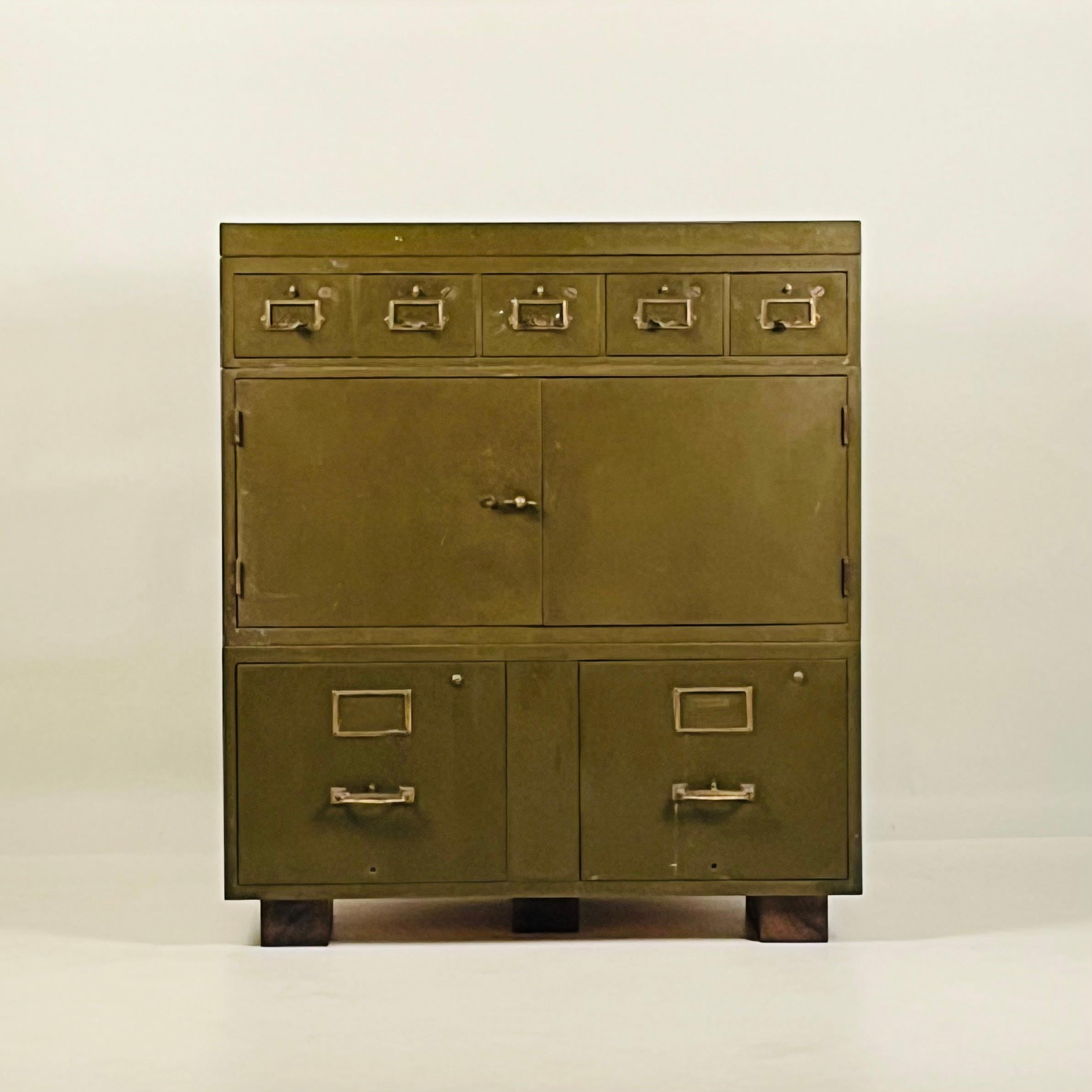 Patinated Industrial Metal Cabinet with gorgeous army green paint and brass details. Stained wood block risers keep it off the ground. 