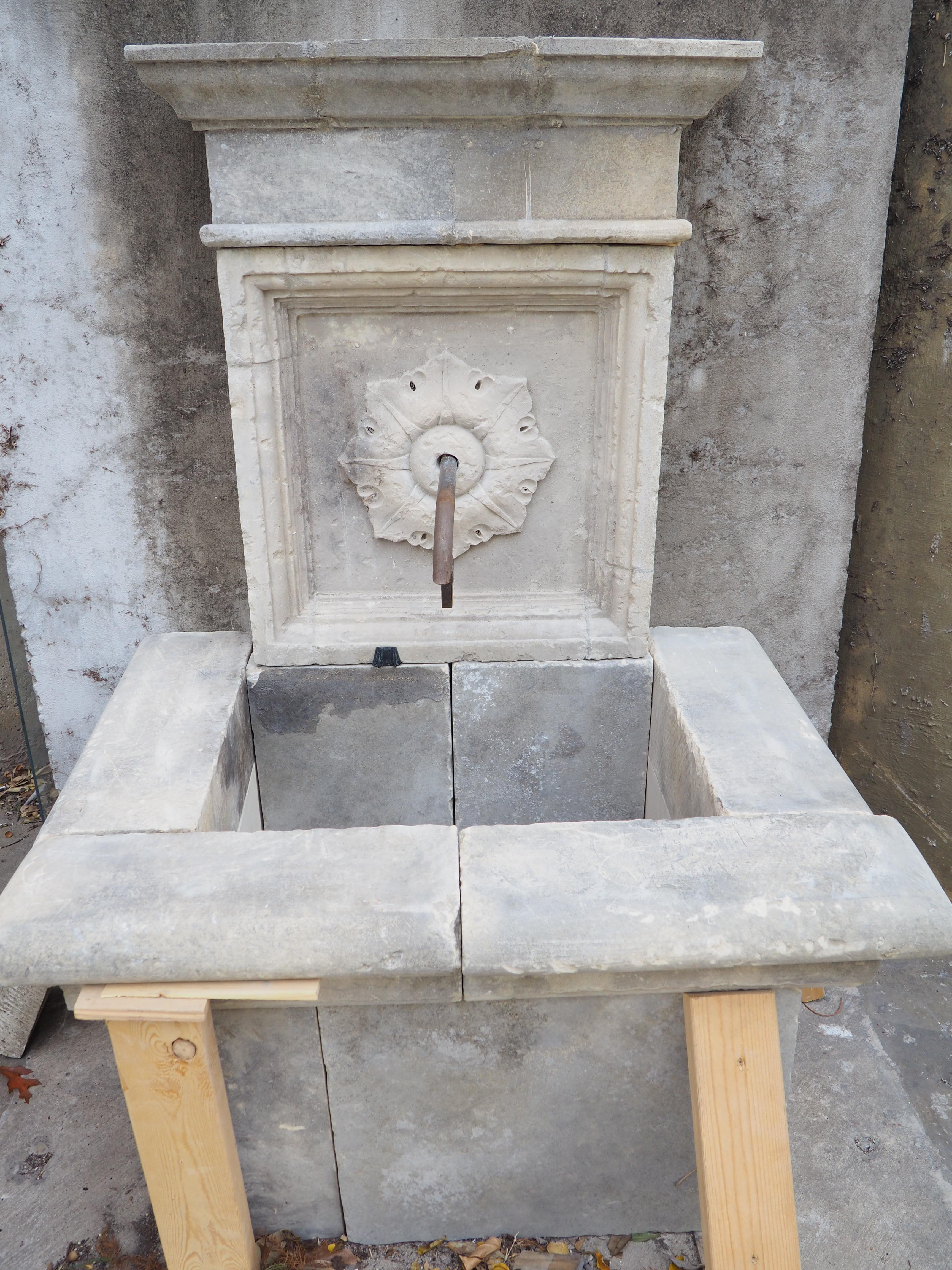 Consisting of 12 pieces of hand-carved limestone, this small patinated wall fountain was produced in Southern Italy. The top cornice features several layers of molding, including quarter round and cavetto edges. Beneath the top section is a square