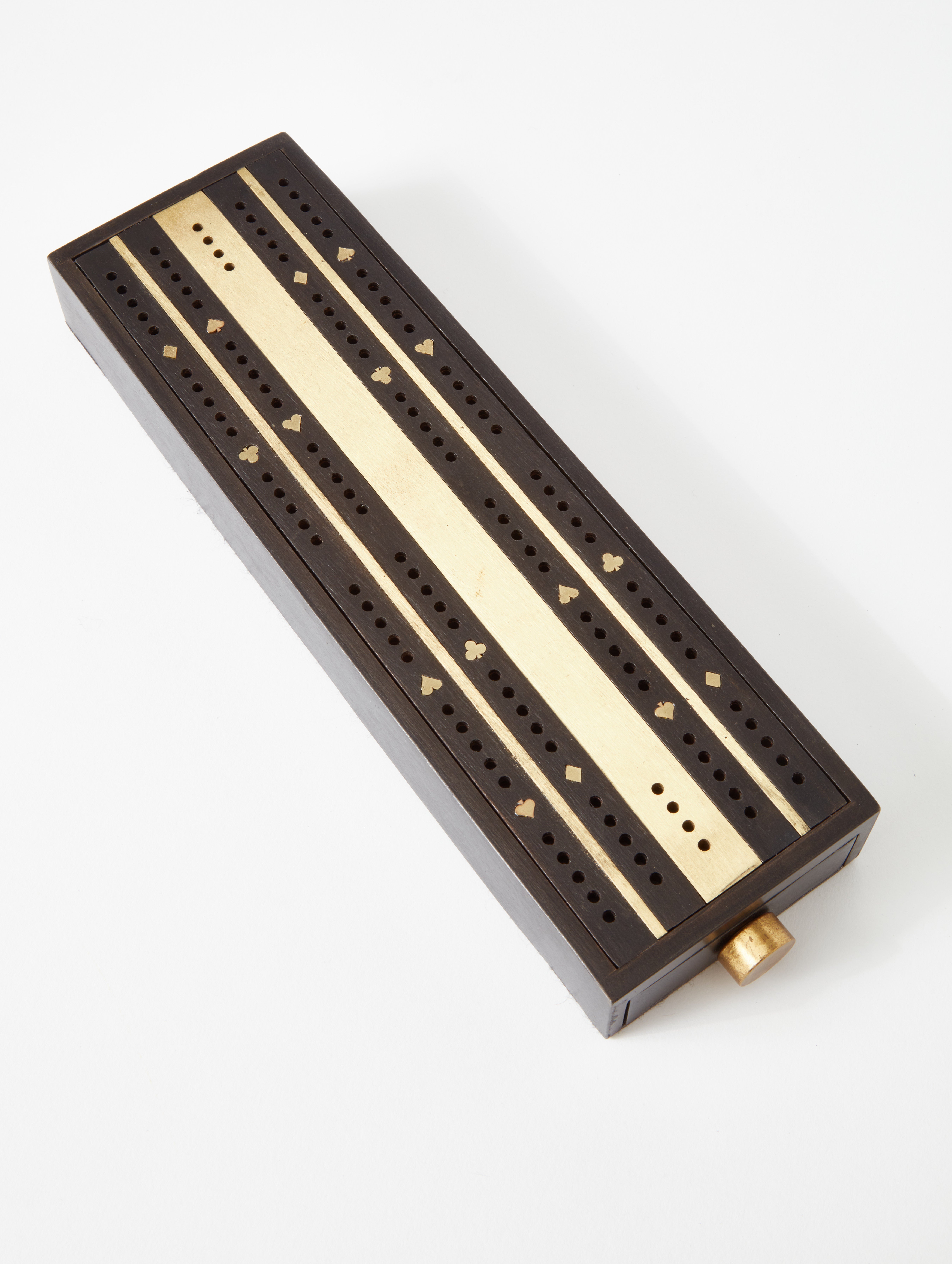 A cribbage board made from brass and steel with intricate inlayed brass details.
A felt-lined drawer on one end holds a deck of cards while the two drawers on the opposite end hold pegs for scoring. Each drawer has magnetic retention to keep them