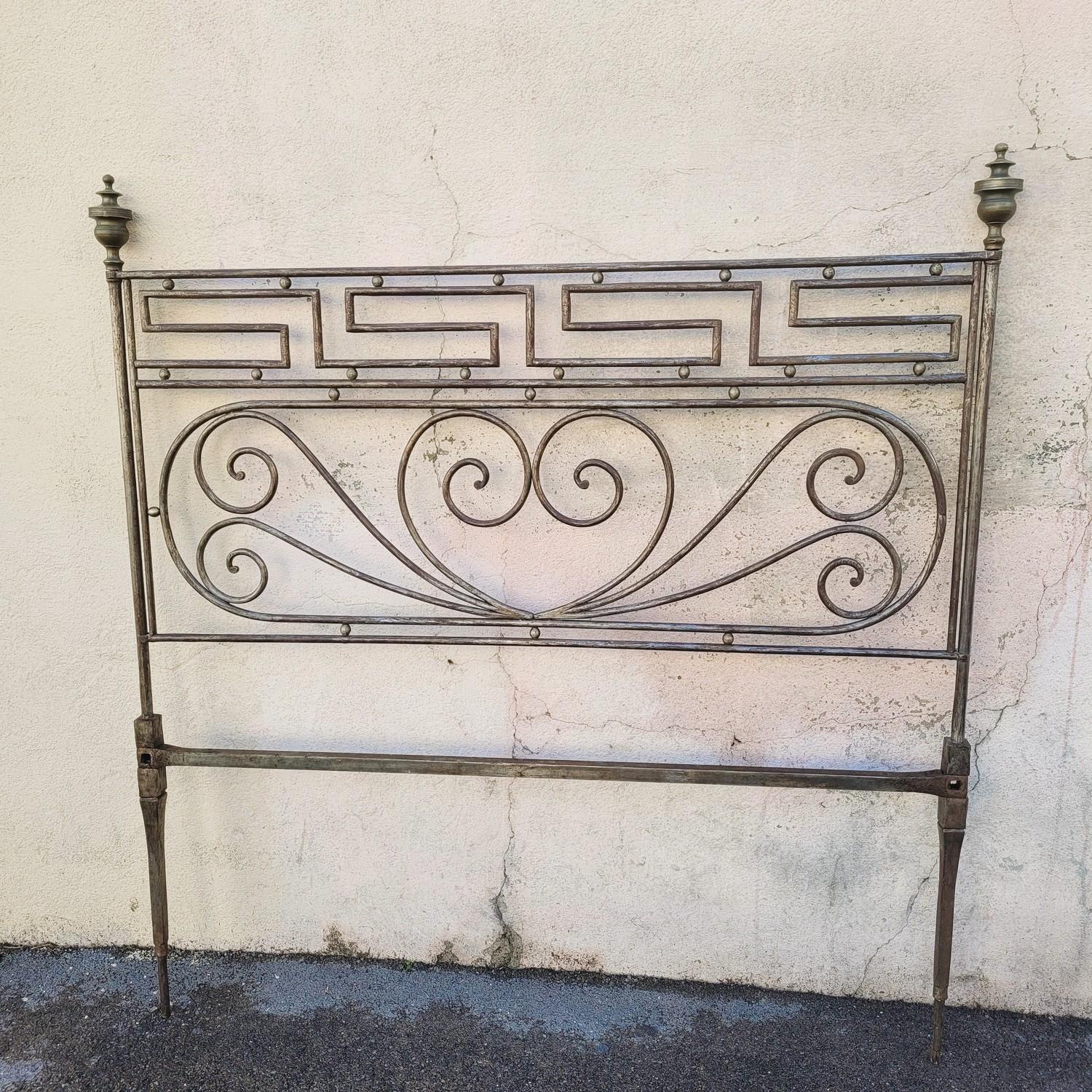 Beau lit en acier patiné, décoré de volutes, d'une frise grecque et se terminant par des toupies en bronze.   

Porte une marque WC entourée d'un cercle.   

Bon état général, usure de la patine, manque 2 petites boules au niveau des volutes. 