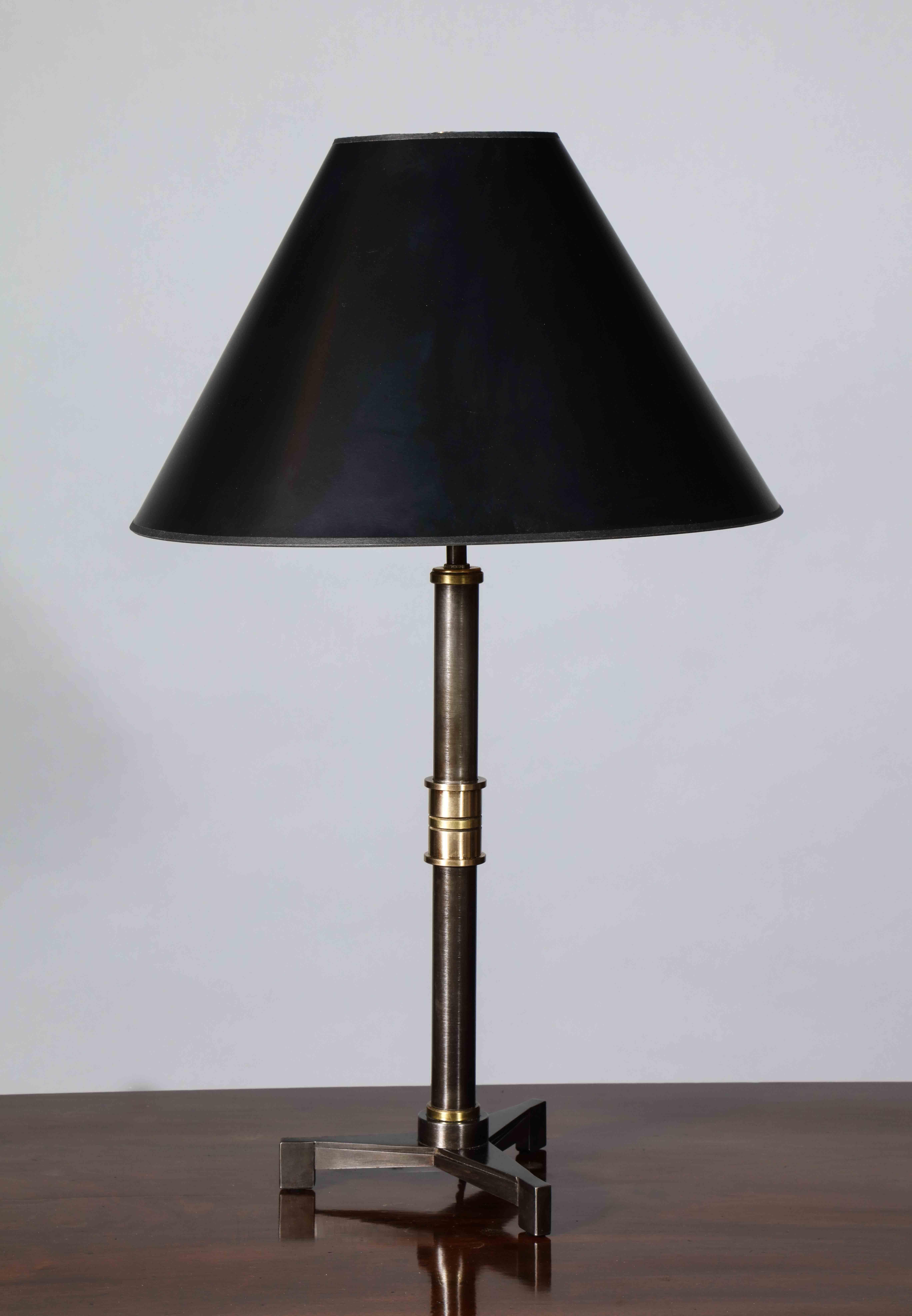 A table lamp with a tri foot base featuring tapered fluting which resonates in the art deco movement. The hilt is realized in a series of subtly contrasting brass and bronze bands. This design is also inspired by the mid-century French Neoclassical