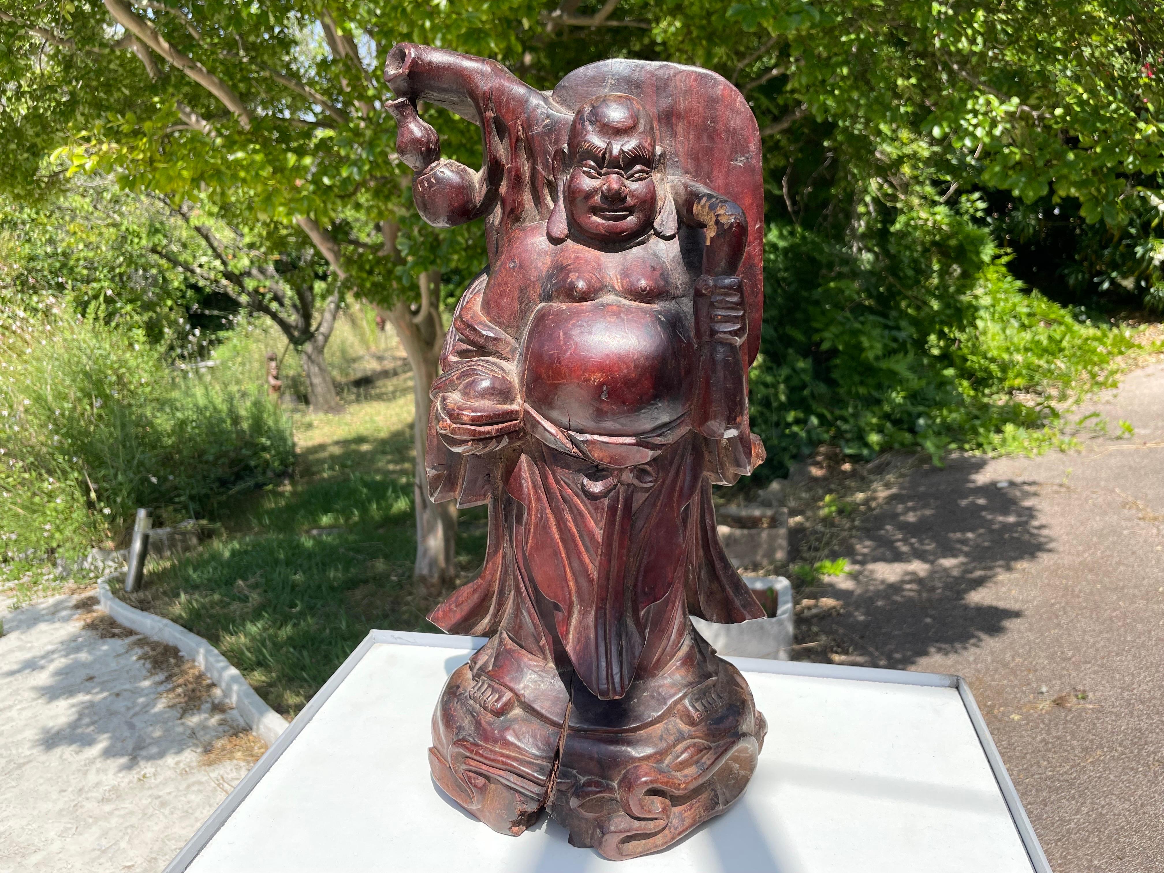 We have a very nice wooden Buddha sculpture. It dates from the early 20th century, and you can see the aging in its beautiful patina. The work of sculpture is very precise and very flexible, it is a quality object. The sculpture is slightly split at