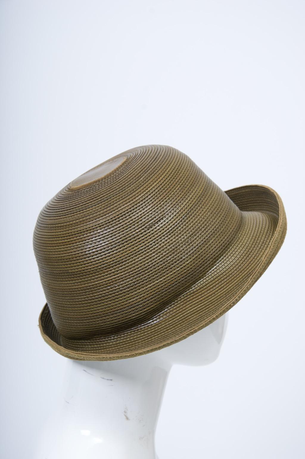 Le chapeau en olive de Patricia Oliver est un peu un trompe-l'œil, car il semble être un chapeau de paille à première vue, mais il est en fait constitué d'étroites bandes de cuir cousues en rond pour simuler la paille, ce qui témoigne d'une