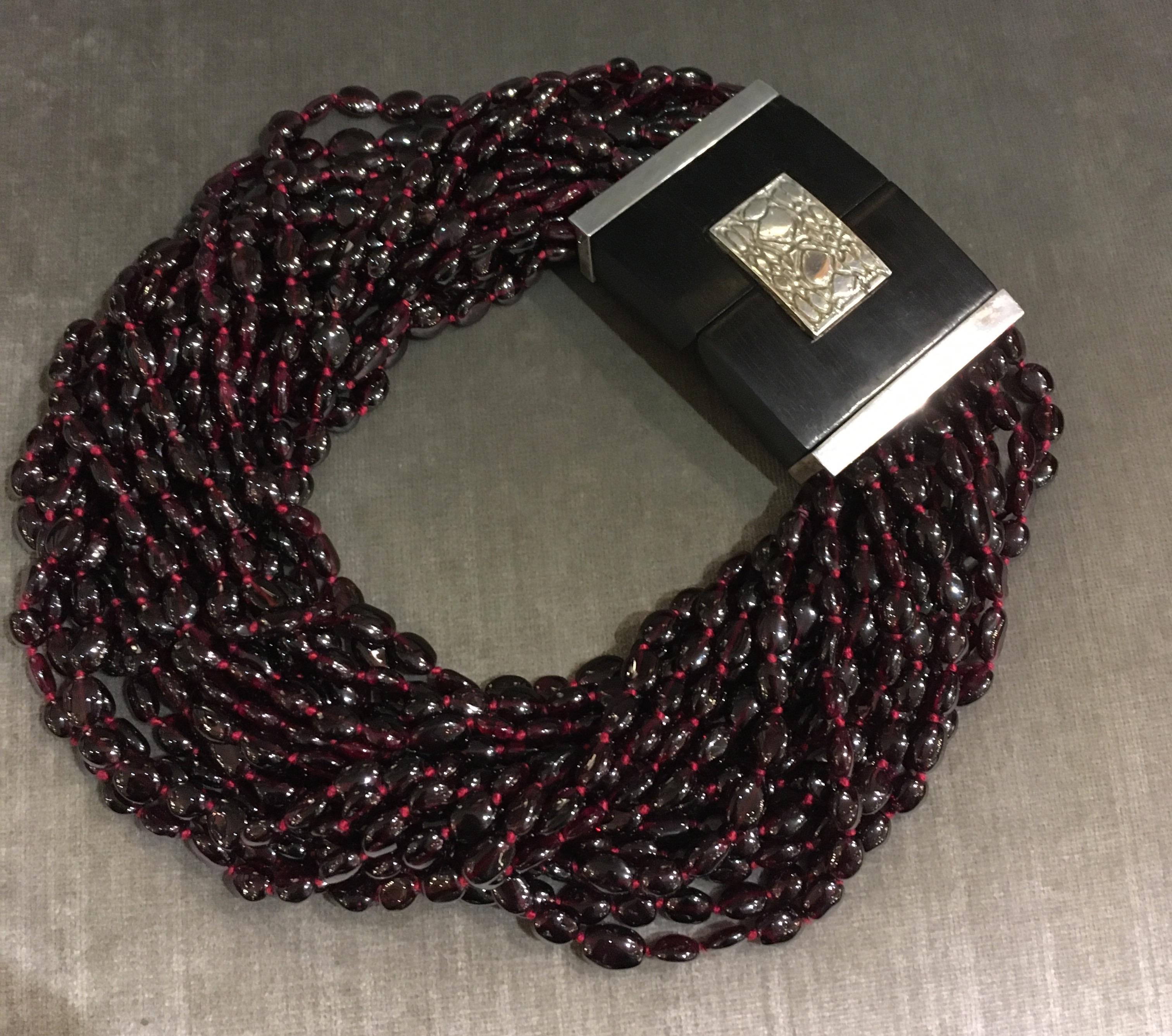 Hand strung garnet beads on silk thread with large decorative ebony and sterling clasp. Artist signature on clasp. Can be worn straight so it sits lower on neck, or beads can be twisted so it sits higher on the neck. Looks beautiful either way.