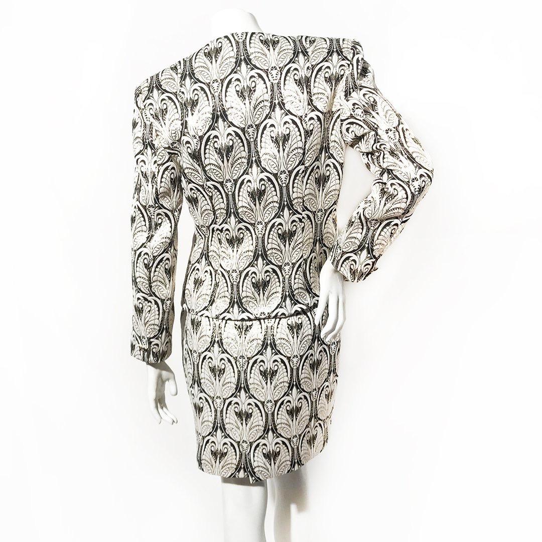 Vintage skirt suit by Patrick Kelly
1988
Black and white brocade print outlined in metallic gold thread
Quilted jacket and mini skirt 
Decorative gold and black crystal buttons on front of jacket 
Single button on jacket cuffs
Deep scoop neck