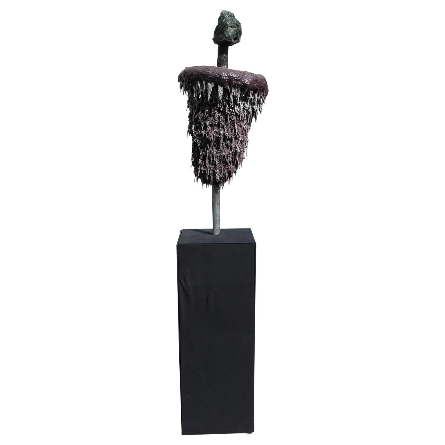Brutalist avant-garde sculpture by artist Patrick McSwain. Three-piece sculpture consisting of a small green toned rock shaped object on a steel tube that goes through a red toned, round, and rough abstracted form that tapers. Sculpture sits on a