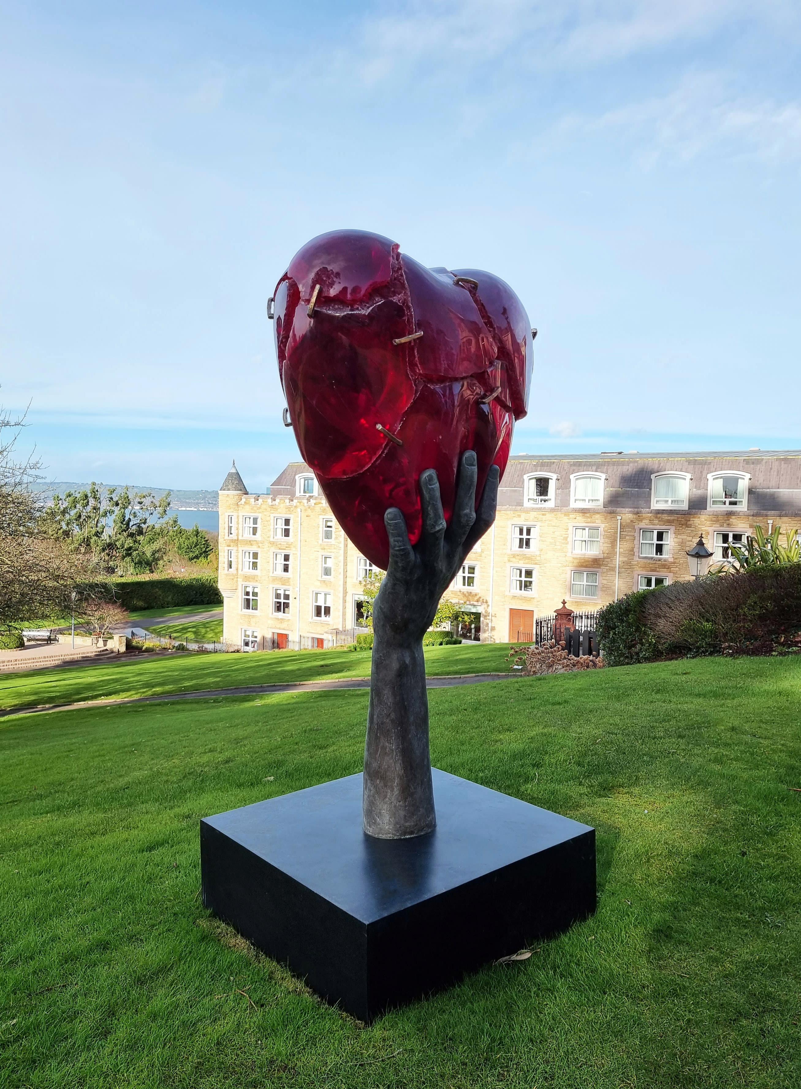 This piece is entitled Heartfelt. It is a large scale outdoor sculpture. The bronze hand holds up a beautiful cracked heart. The crystalline art resin is purposely cracked using a chemical reaction. Then O'Reilly uses bronze staples to mend the