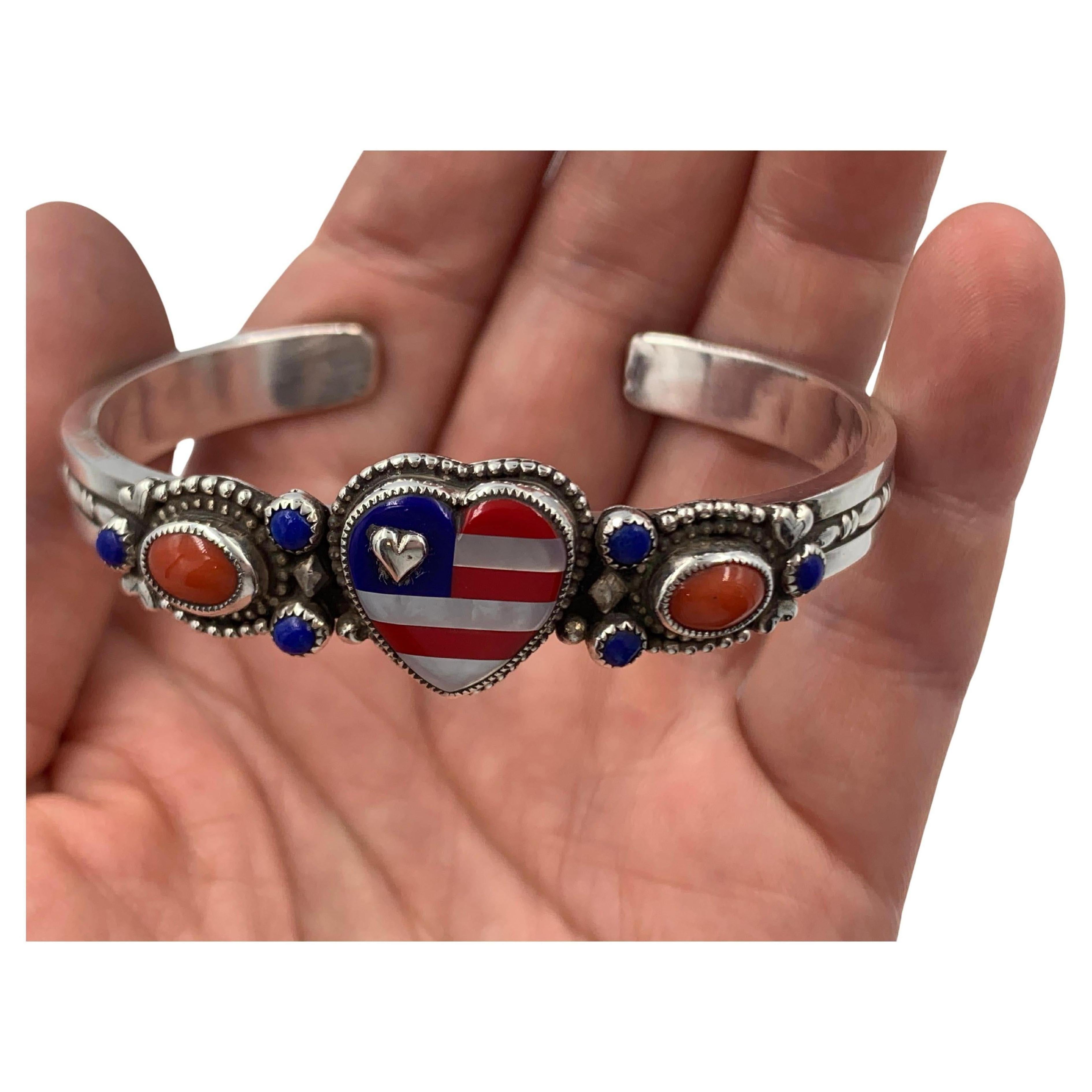 Sterling Silver cuff created with a beautiful inlayed heart showing the USA flag design and colors. 
The Heart is inlayed with semi-precious Mother-of-pearl, Blue Lapis, and Red Coral gemstones.
Flanking each side of the Heart are Lapis and Coral