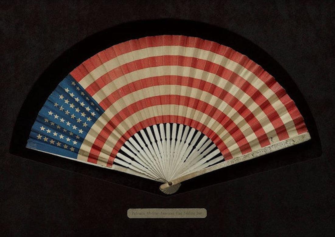 Presented is a printed folding fan featuring the American Flag, which dates to the early 20th century. With 48 printed stars on the fan’s canton, the fan celebrates New Mexico and Arizona statehood. The fan’s design is completed with 13 alternating