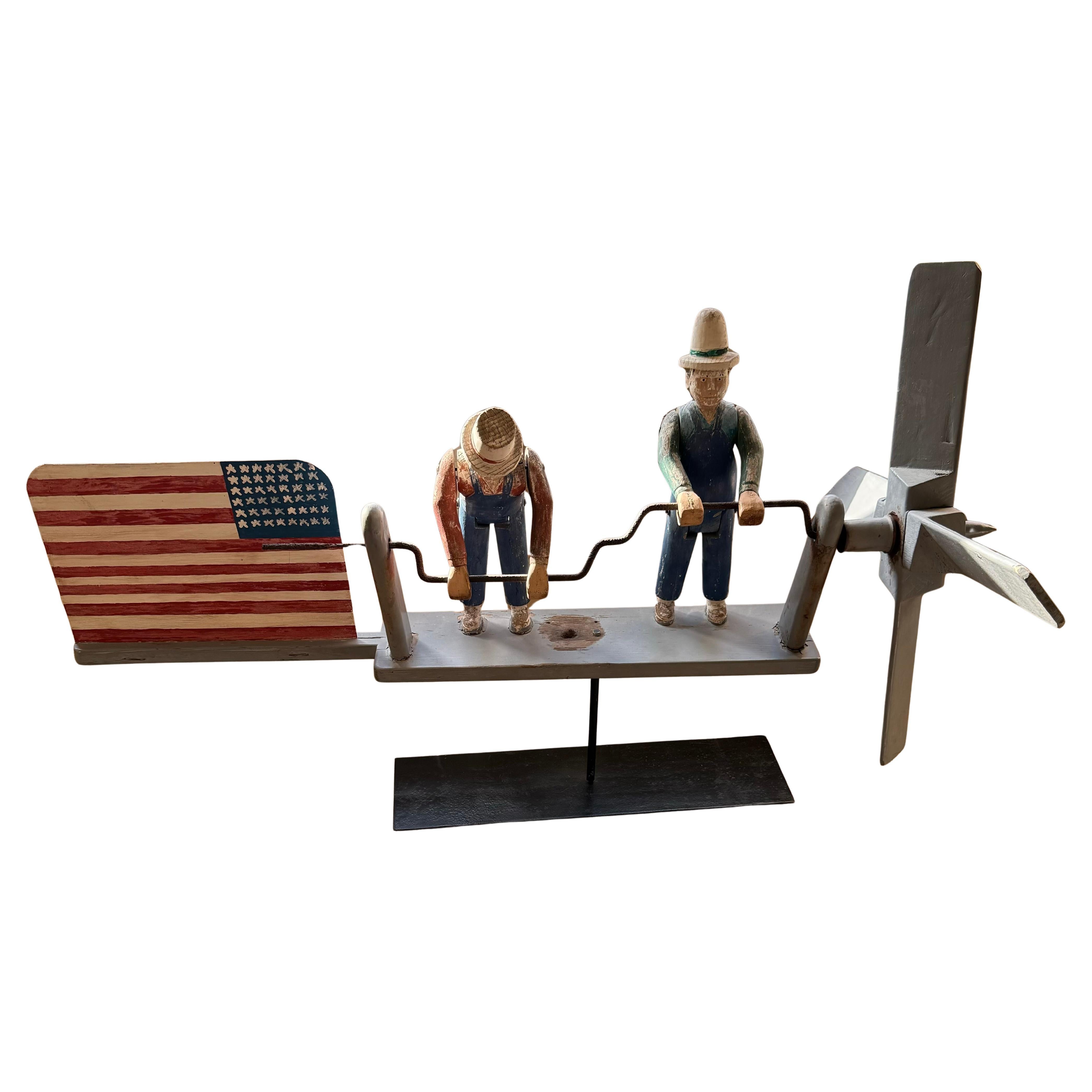 Feiern Sie die amerikanische Handwerkskunst mit diesem charmanten patriotischen Kreisel von 1940. Die aus Holz und Metall gefertigte Figur zeigt zwei Männer und eine amerikanische Flagge, die einen nostalgischen und patriotischen Geist einfangen.