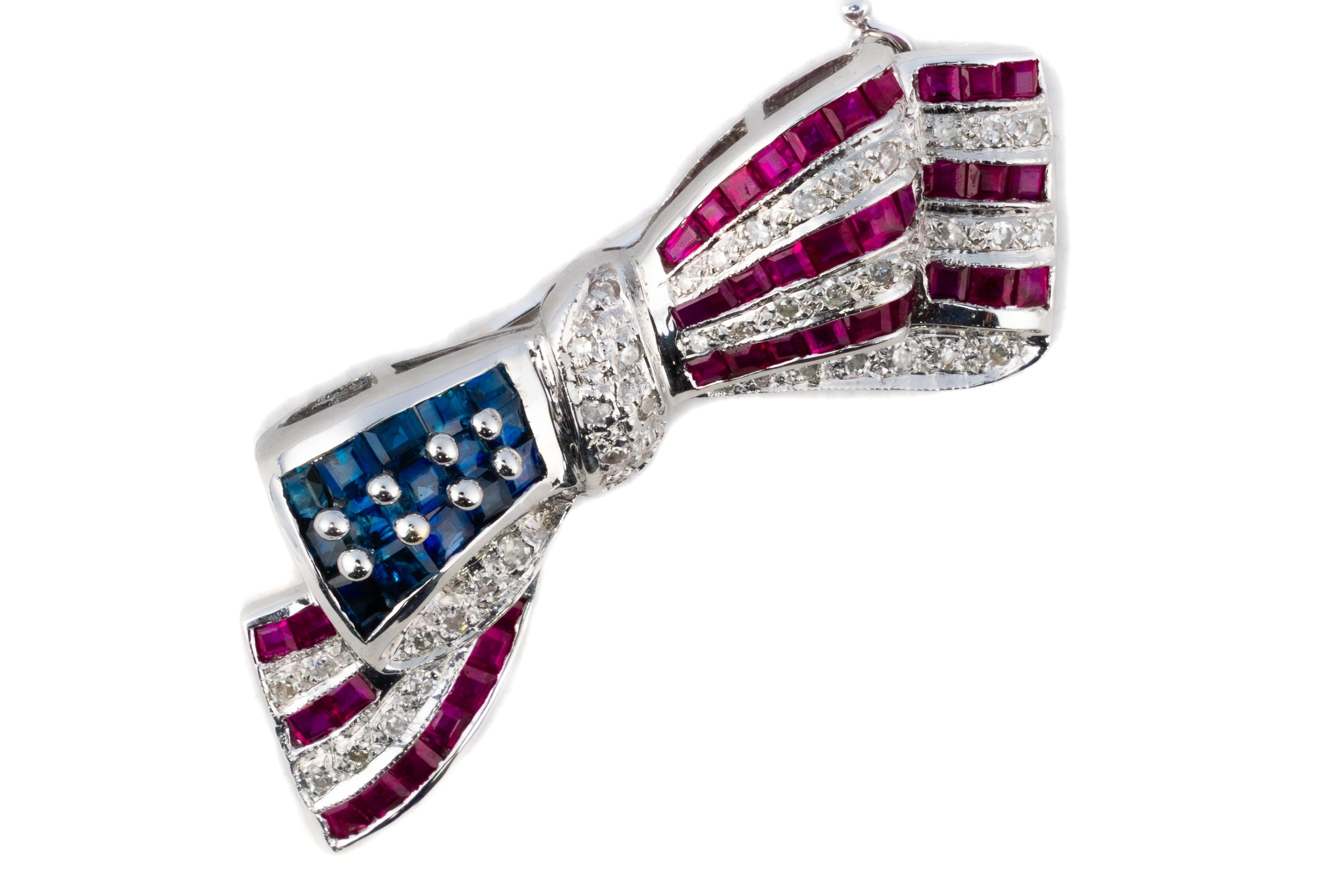 Patriotische Rubin-, Saphir- und Diamant-Brosche mit Flaggenband

Beschreibung:
Diese lebendige Brosche in Form eines fließenden Bandes, das an die amerikanische Flagge erinnert, ist mit Reihen von Rubinen und Diamanten in Kanalfassung besetzt. Eine