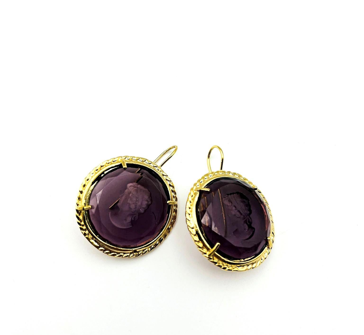 Patrizia Dalinana Earrings in 24 KT gilded bronze with carved, hand-ground Murano glass depicting an ancient Roman woman's head in amethyst color. To wear it to the ear, a suitably shaped bronze wire is used. To fix the stones to our jewels,