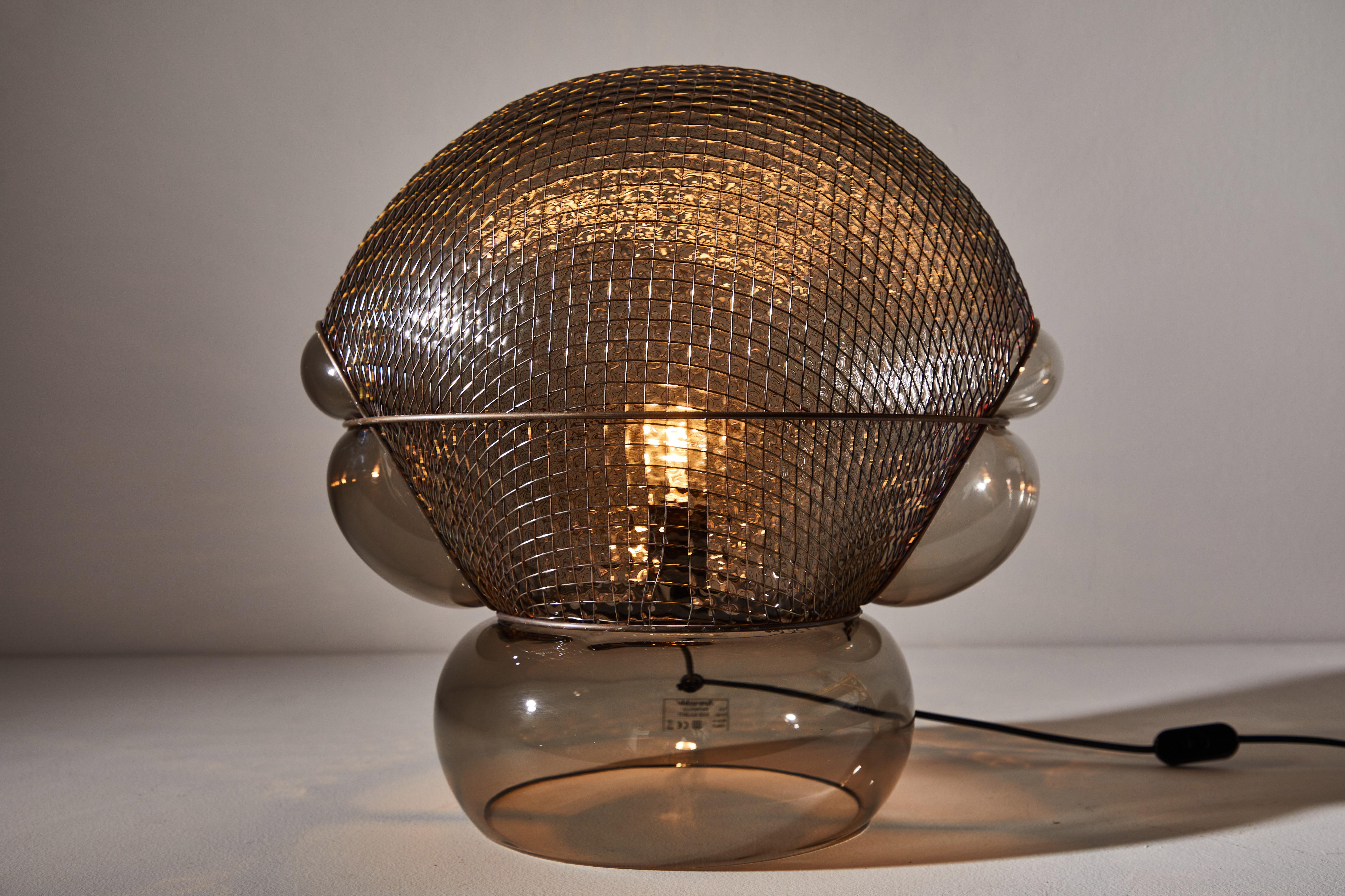 Patroclo table lamp by Gae Aulenti originally designed in 1975. Current vintage deadstock edition produced in Italy by Artemide. Comes with full range dimmer on the hand switch. Smoke colored blown glass and steel mesh. Maintains original Artemide